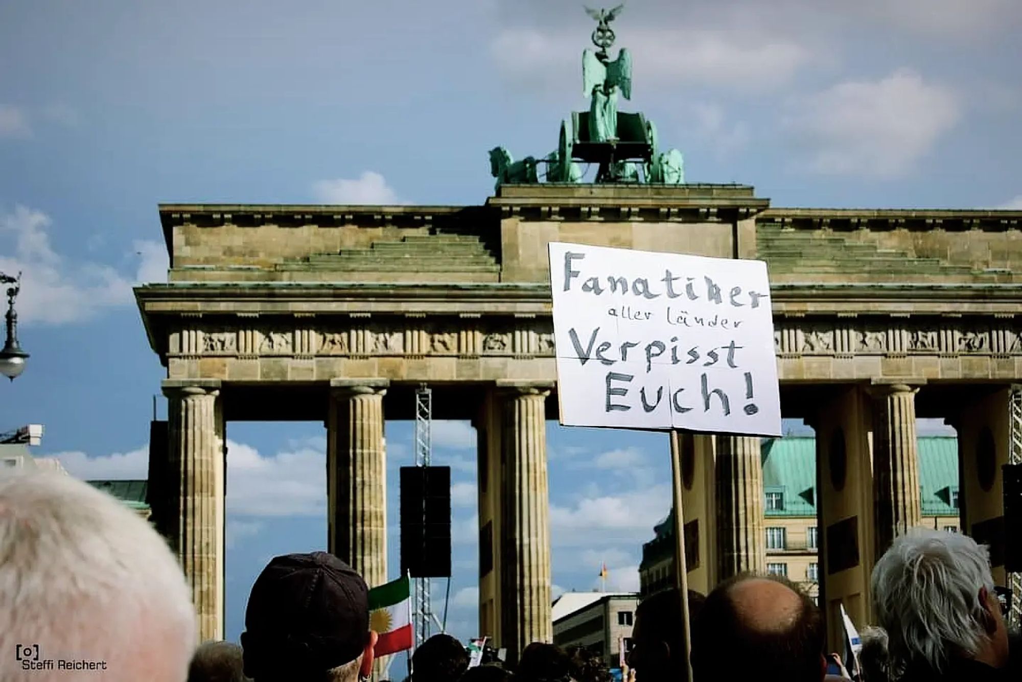 Menschen vor dem Brandenburger Tor mit Plakat, auf dem steht: "Fanatiker aller Länder verpisst euch".