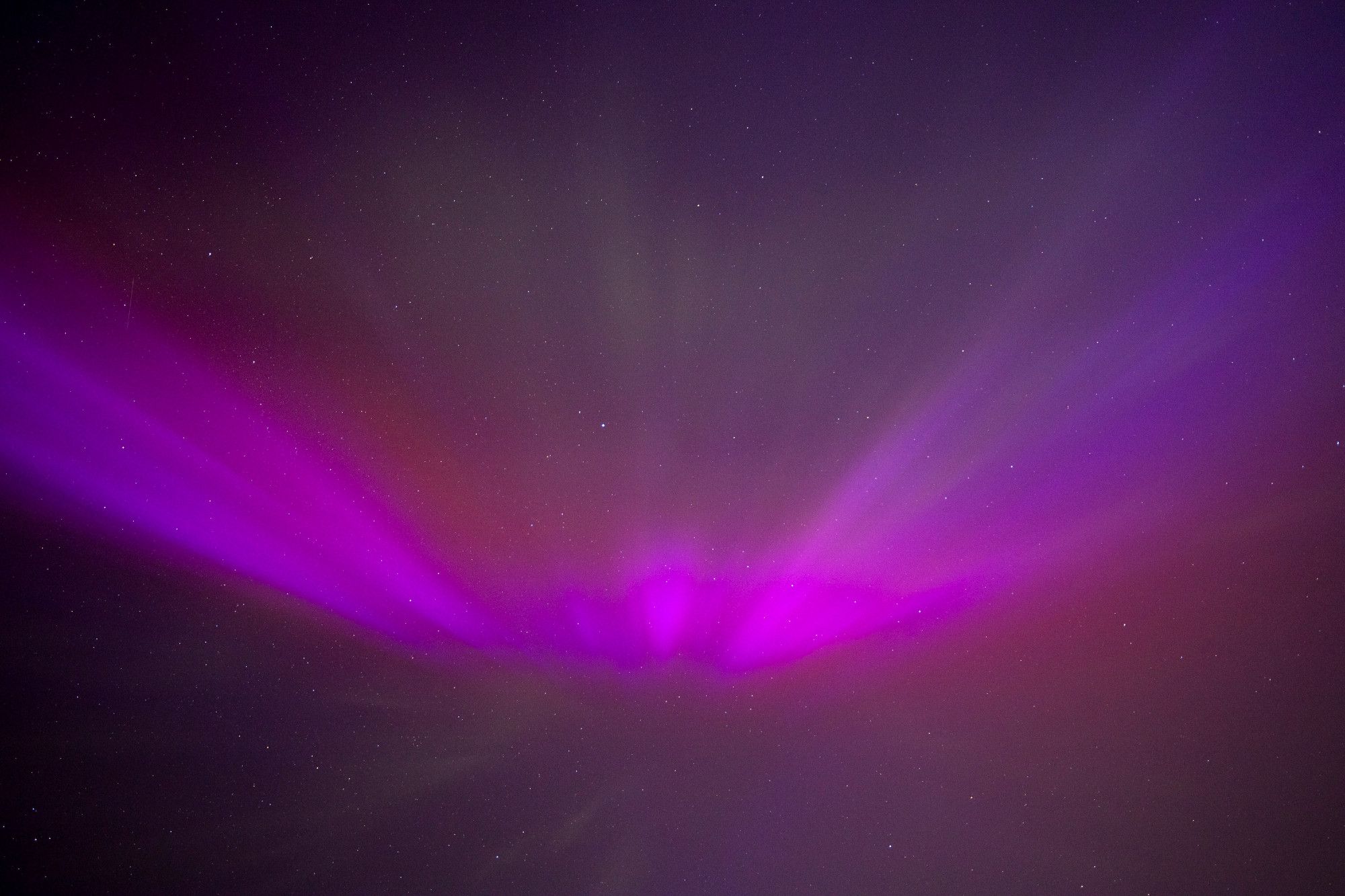 Looking straight up into an aurora-filled night sky, bold and deep purples stretching overhead from one end of the frame to the other, like arms of an angel reaching out to hold you. Scattered bits of red are seen around the purple, especially at center