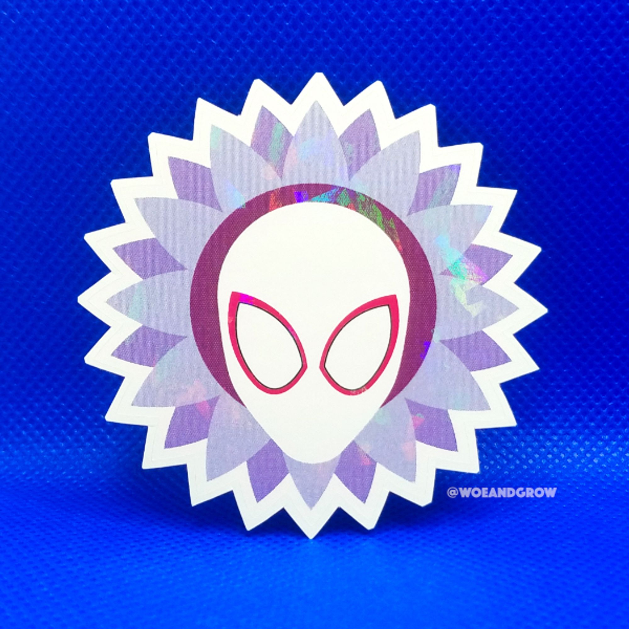 Photo of my Spiderverse Sunflower holographic sticker: a masked Gwen Stacy Spiderwoman encompassed by a purple sunflower.