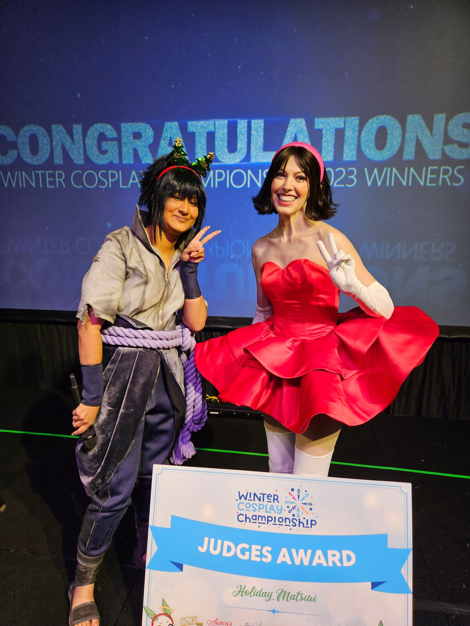 A photo of me cosplaying Mima from Perfect Blue standing next to KiyaNocturne, another cosplayer dressed as Sasuke. We're posing with the Judges Award she gave me last year at Holiday Matsuri.