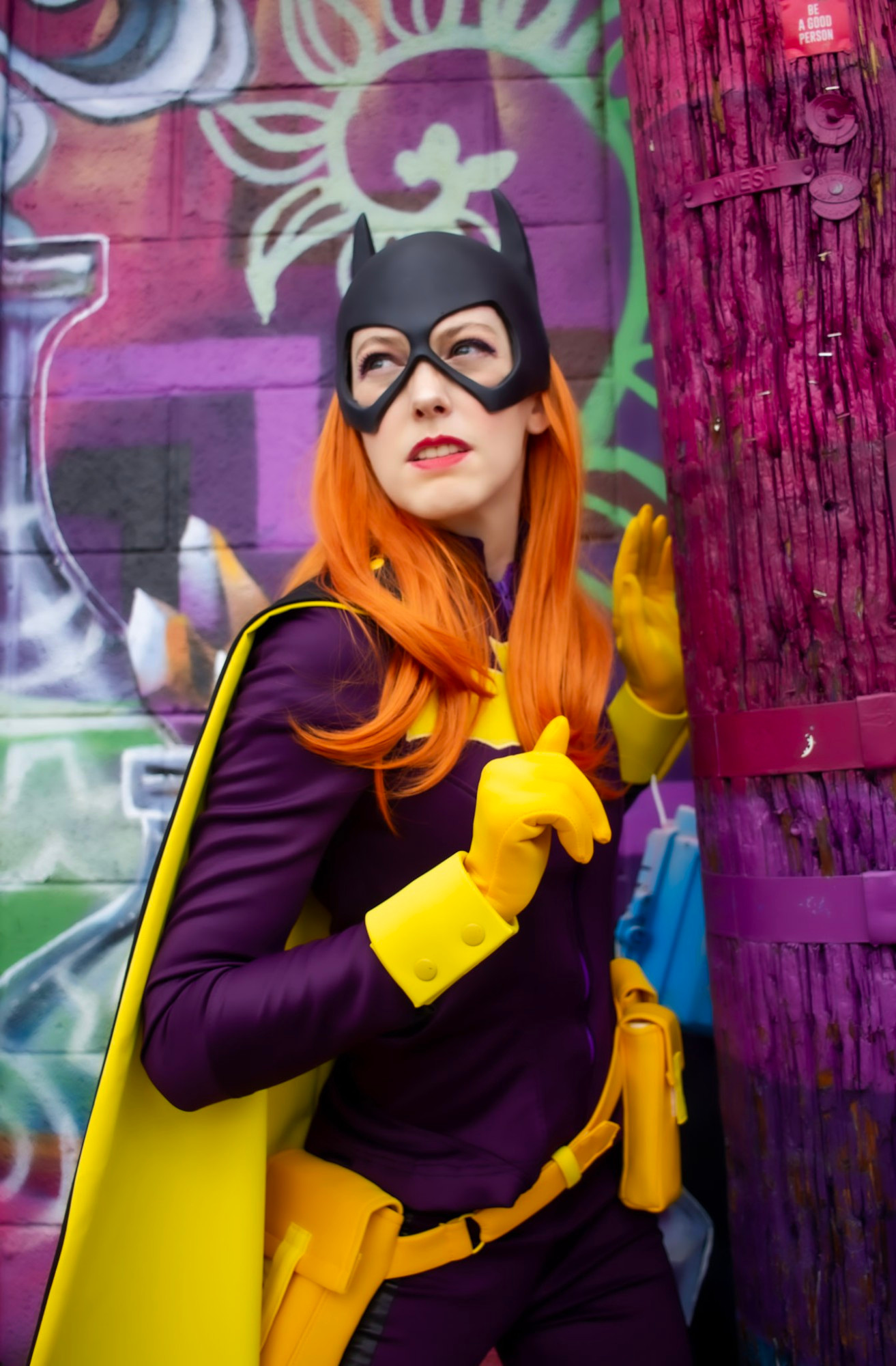 A photo of me dressed as Batgirl standing in front of a bright and vibrant piece of graffiti art.