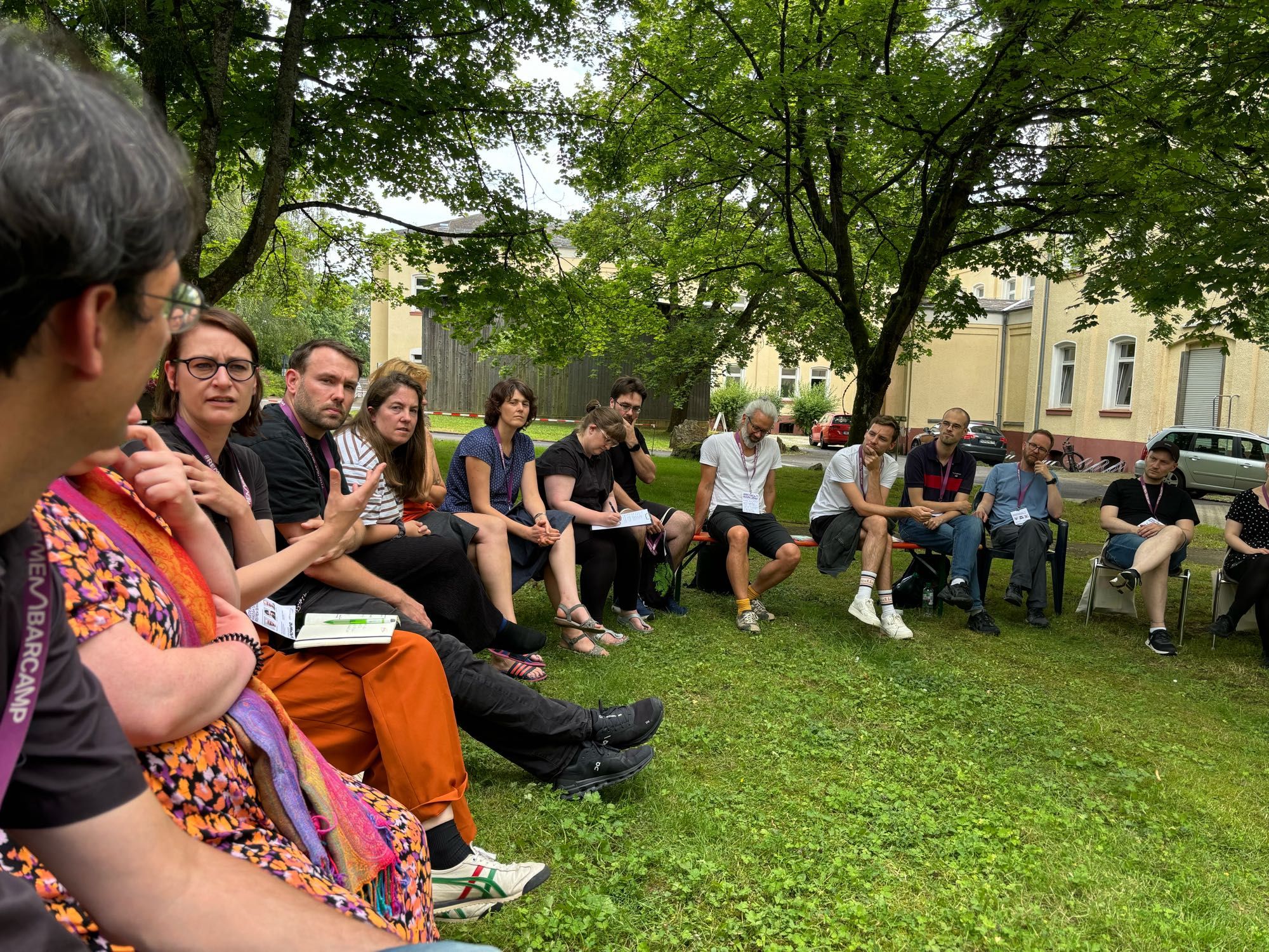 Eine Gruppe von Personen sitzt auf Stühlen im Kreis auf dem Rasen