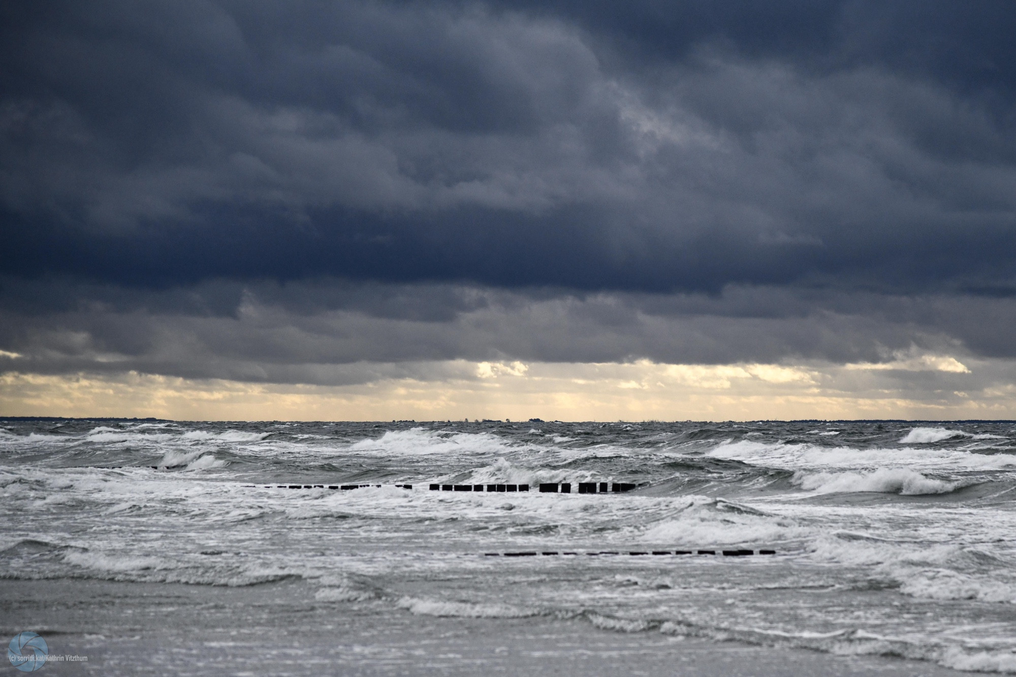 Dunkle Regenwolken über der Ostsee Richtung Darß. Ein leichter Sonnenstreifen ist erkennbar. Die Wellen sind schon ziemlich sturmgeprägt.