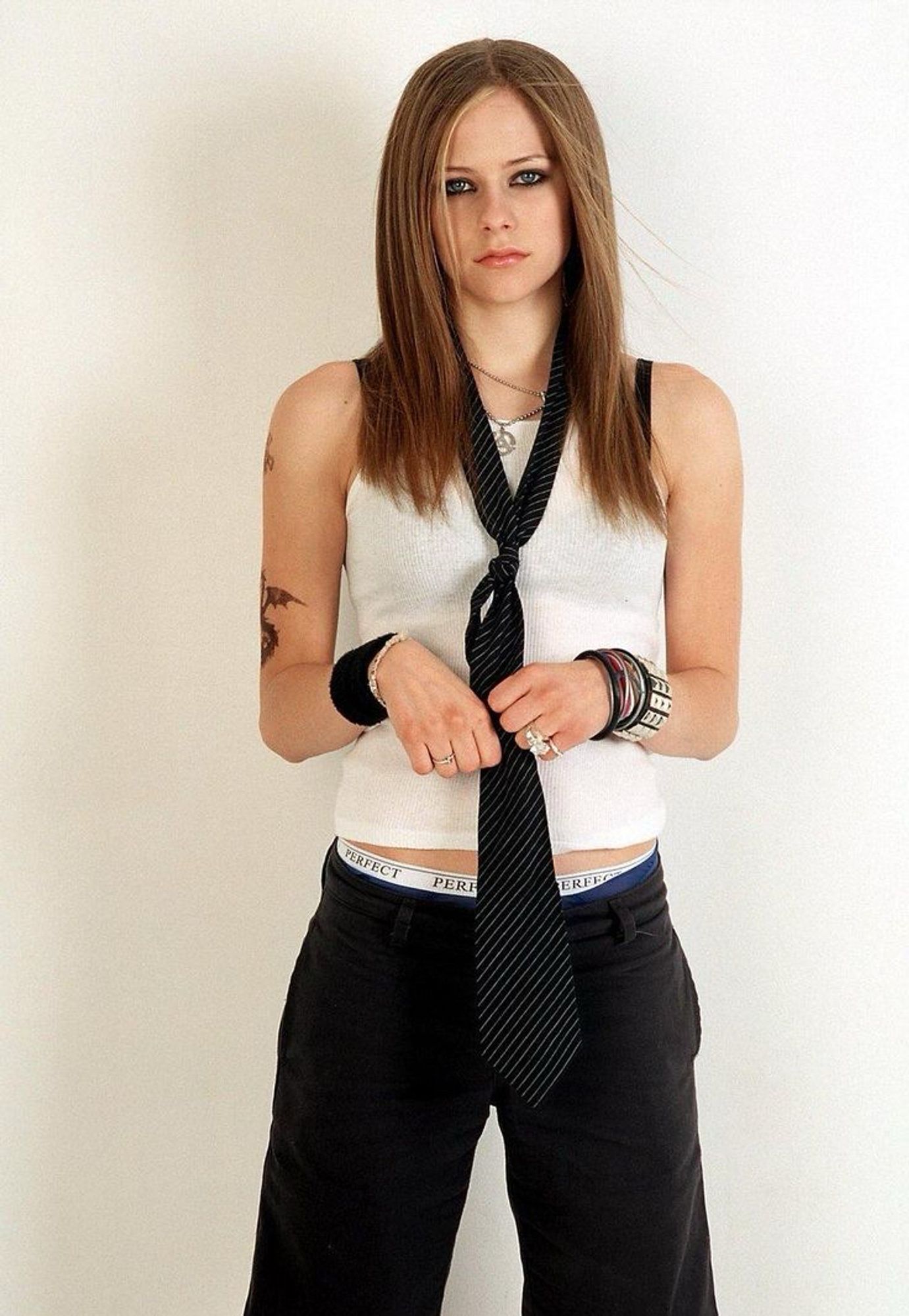 Avril Lavigne in a tank top and a neck tie loosely tied around her neck like a necklace, black pants