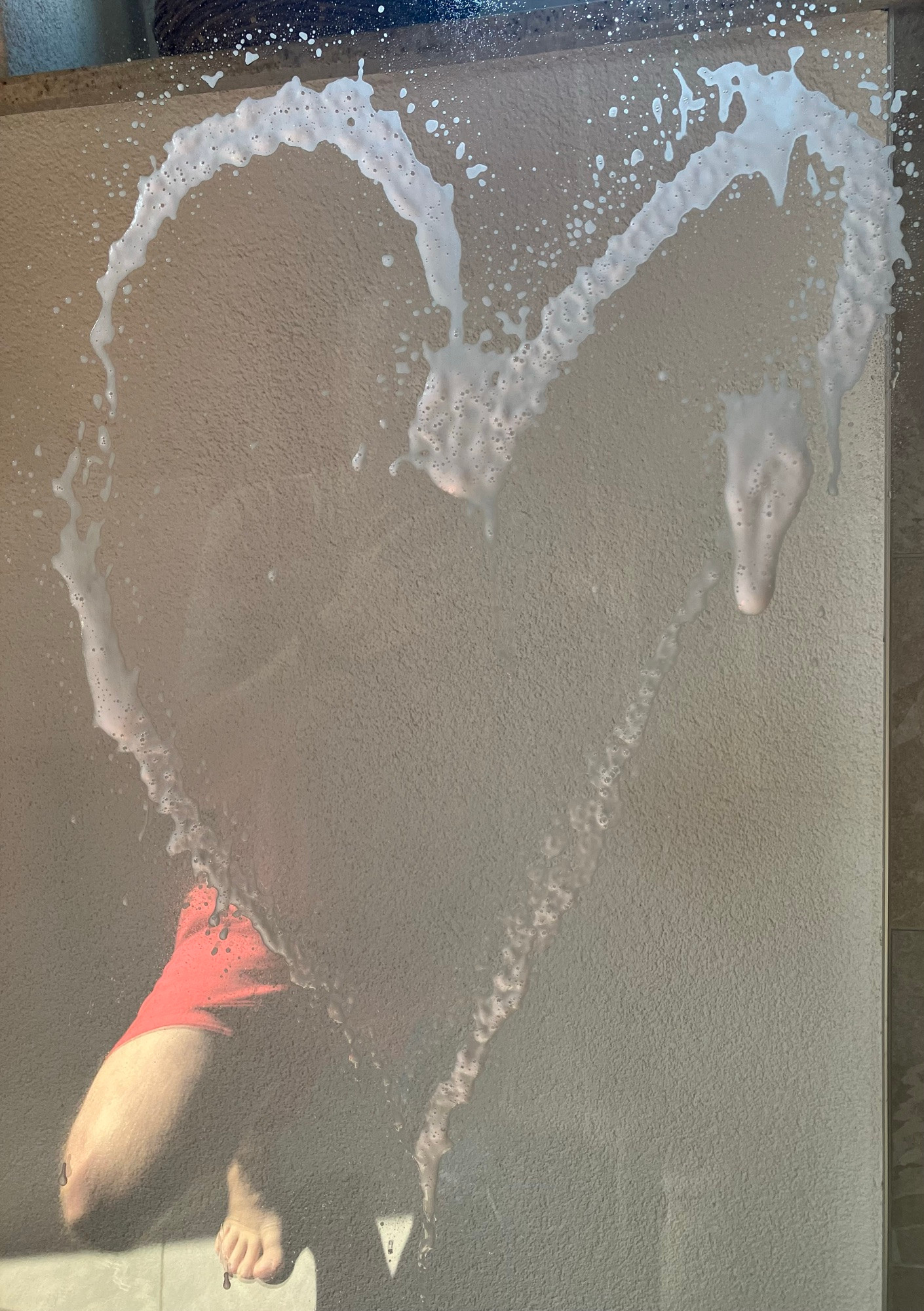 Ein aufgesprühtes Herz aus Glasreiniger auf einer Glastür.