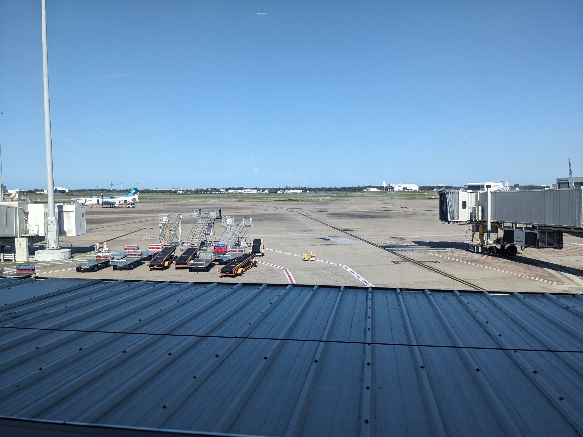 view of the airport tarmac from inside the Brisbane domestic terminal. luggage loaders, Skybridges, hangers in the distance