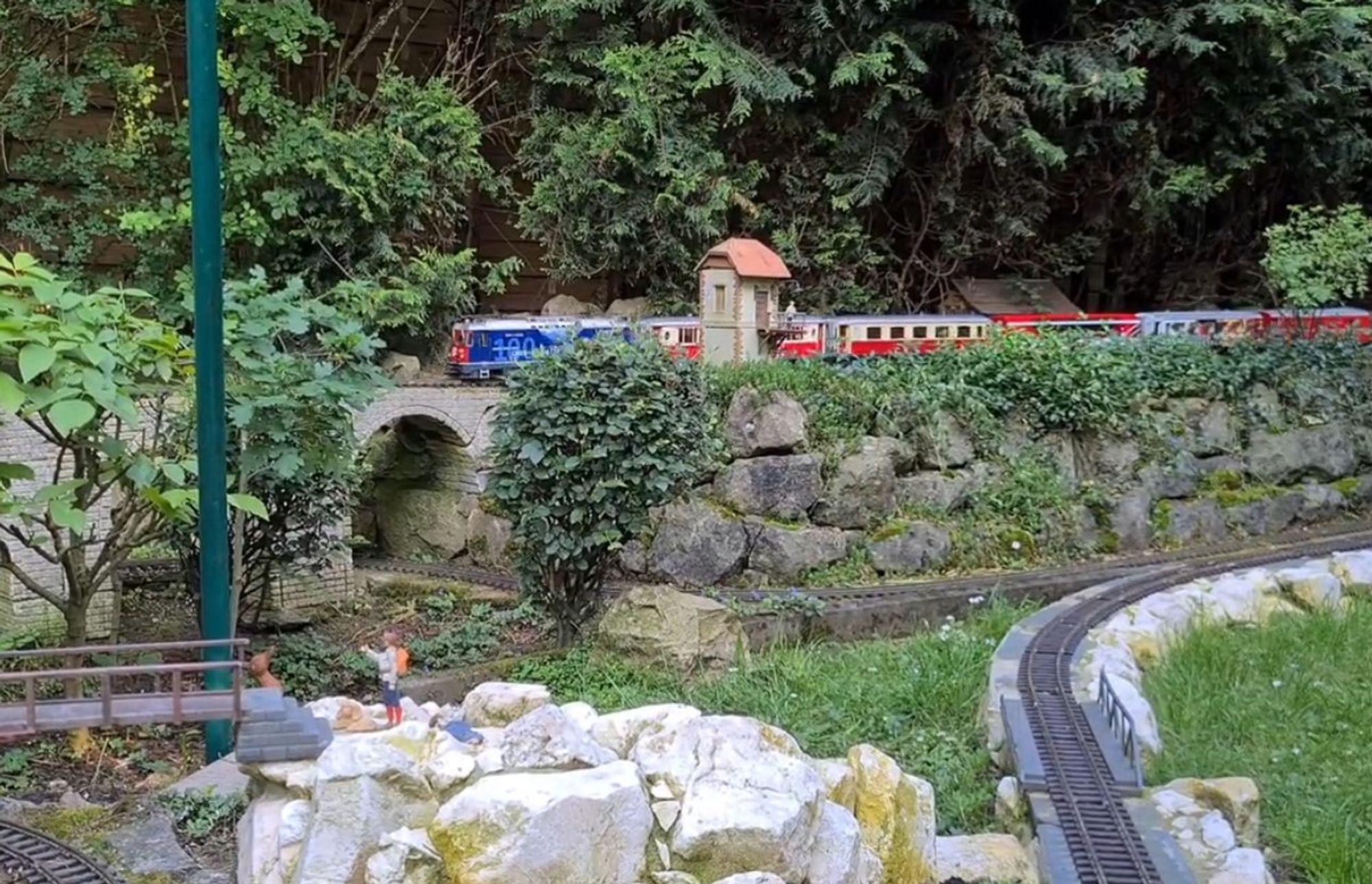 A Piko-rail garden railway with a Swiss rail train going by in the background.