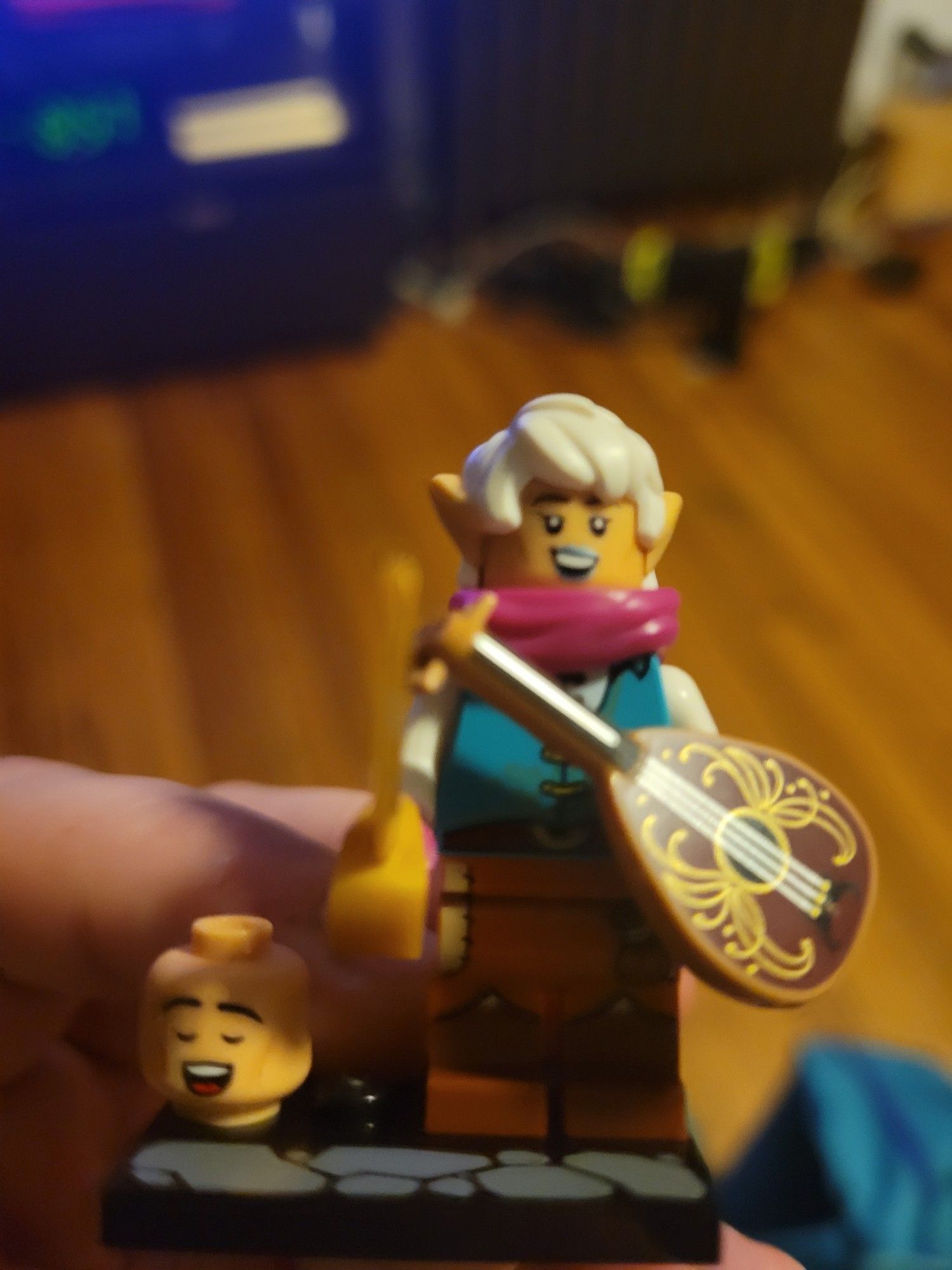 The elven bard from the Lego Dungeons & Dragons Minifigure collection. It comes with both male and female heads; the female head is on and the male head is next to the figure. The figure itself has brown leggings, a teal vest, a magenta scarf, a lute, and a golden cutlass.