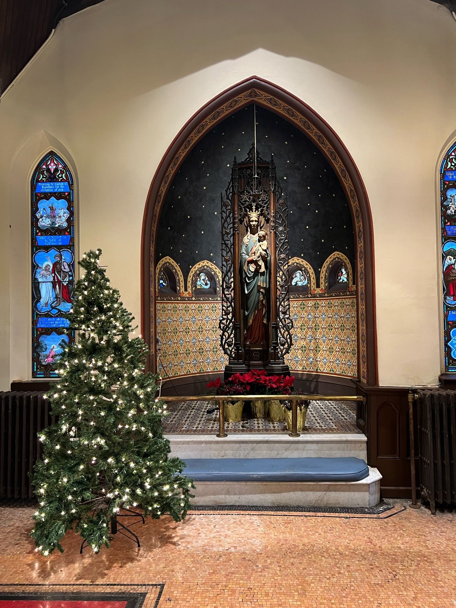 The Virgin Mary in a niche-shaped small chapel, with Christmas tree & flowers.