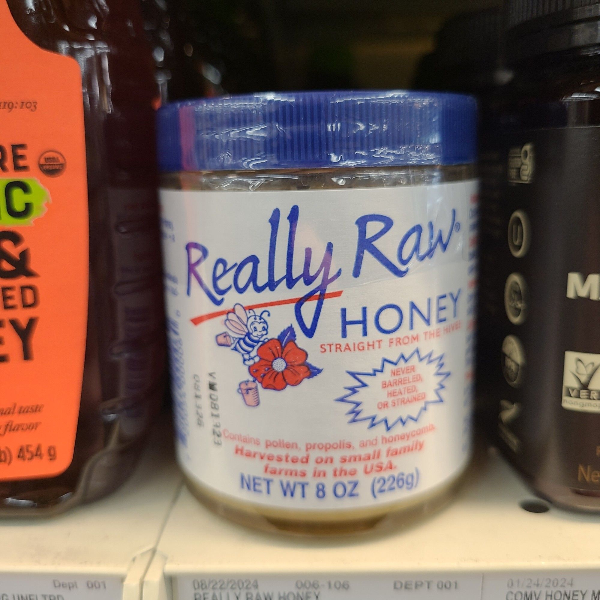 A glass jar of honey with a blue lid sitting on a grocery store shelf. The brand name is Really Raw.