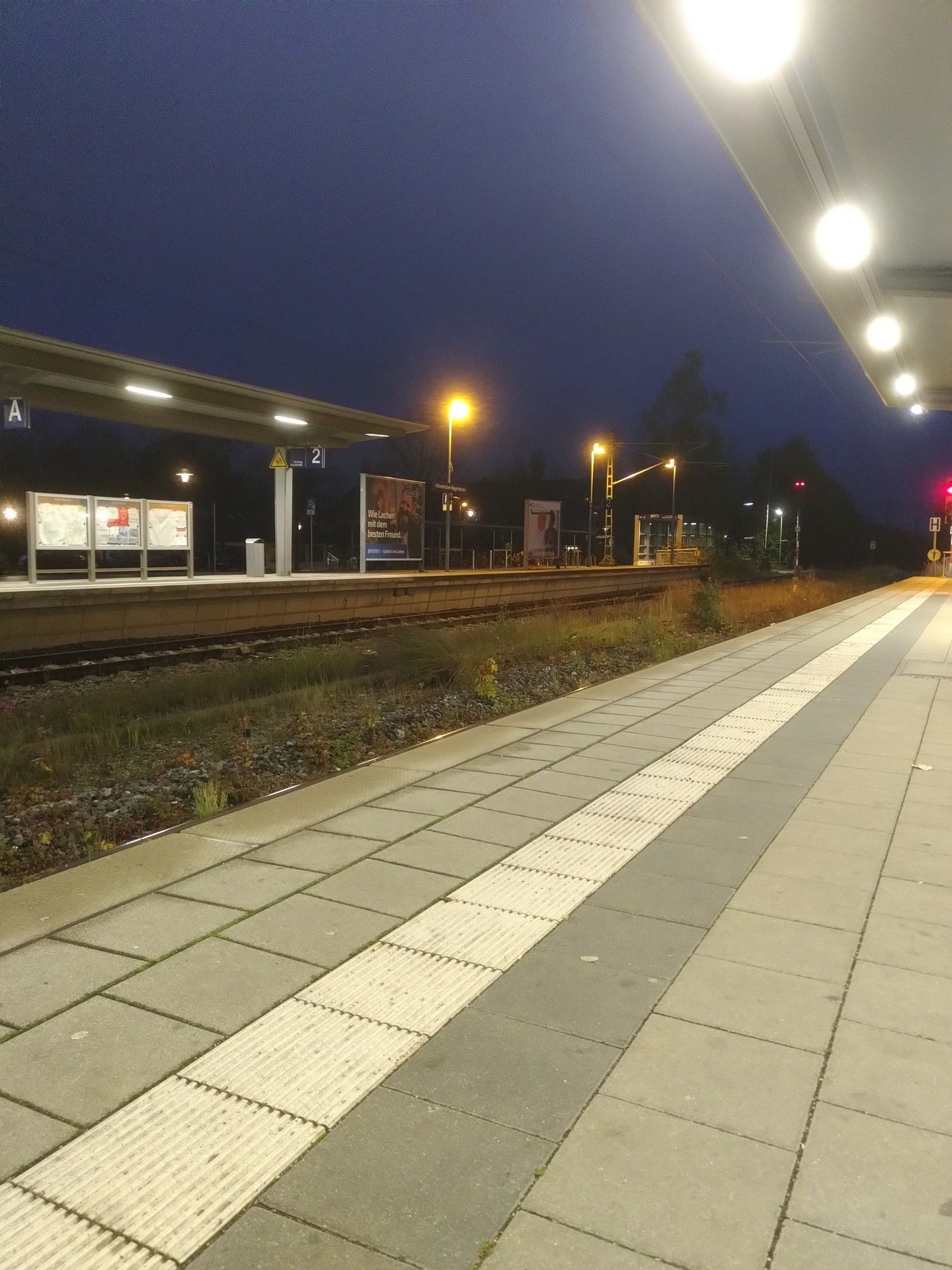 Ein leerer S-Bahnhof im Dunkel. Der Himmel ist tiefblau und gelb und weiß leuchtende Lampen erhellen Bahnhof und Gleise.