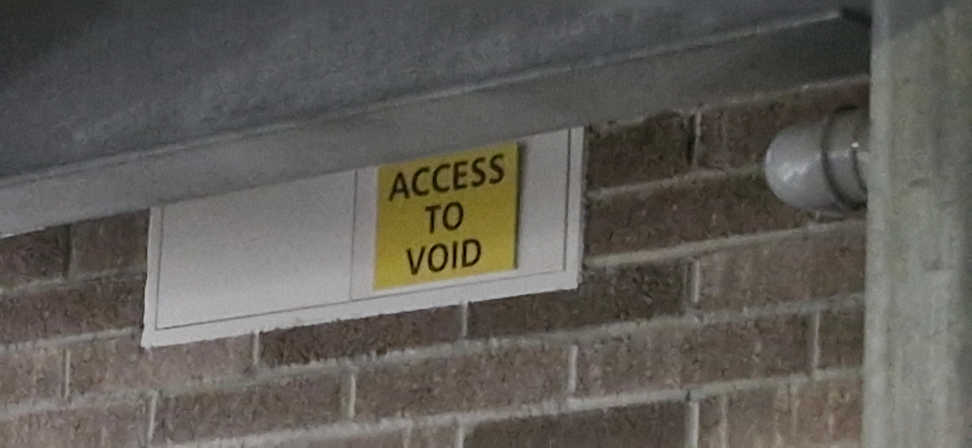 A yellow sign reading "ACCESS TO VOID" in black text fixed to a brick wall.