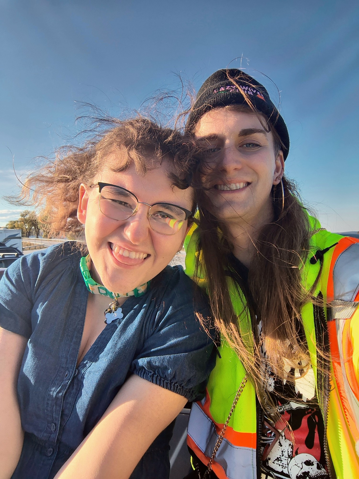 Colie and Rayna smiling at the camera. They are outside, sitting under a clear sky with their hair blowing in the wind, and they look happy