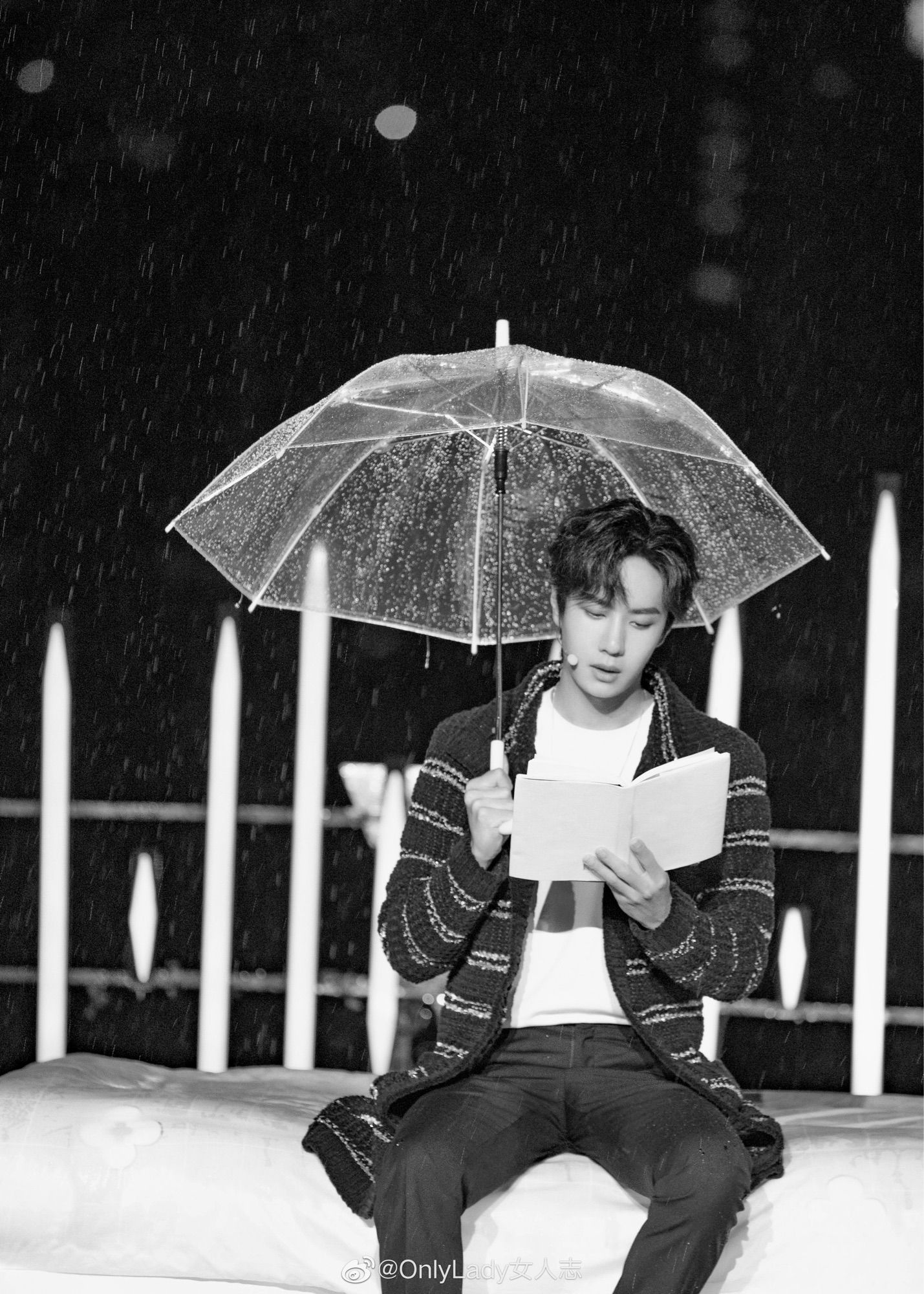 b&w shins up shot of the child from his Hunan TV Young Forever stage, sitting on a white bed, ‘rain’ pouring down, reading from a book and holding a clear plastic umbrella beaded with droplets, wearing dark (blue) dress trousers, a white tee, a rather nice long line Chanel cardie, dark (blue) with a pattern of light (gold thread) horizontal parallel lines, a long-ish delicate chain necklace, and a head mic, beautiful little face serene, eyes downcast as he reads, looking too soft and beautiful for words, and jesus god, someone pay him to read, preferably Le Petit Prince, but i’d pay good money to listen to him reading the yellow pages, because his voice is like the softest silk velvet. 
*sigh*
Damn the child. 
WYB