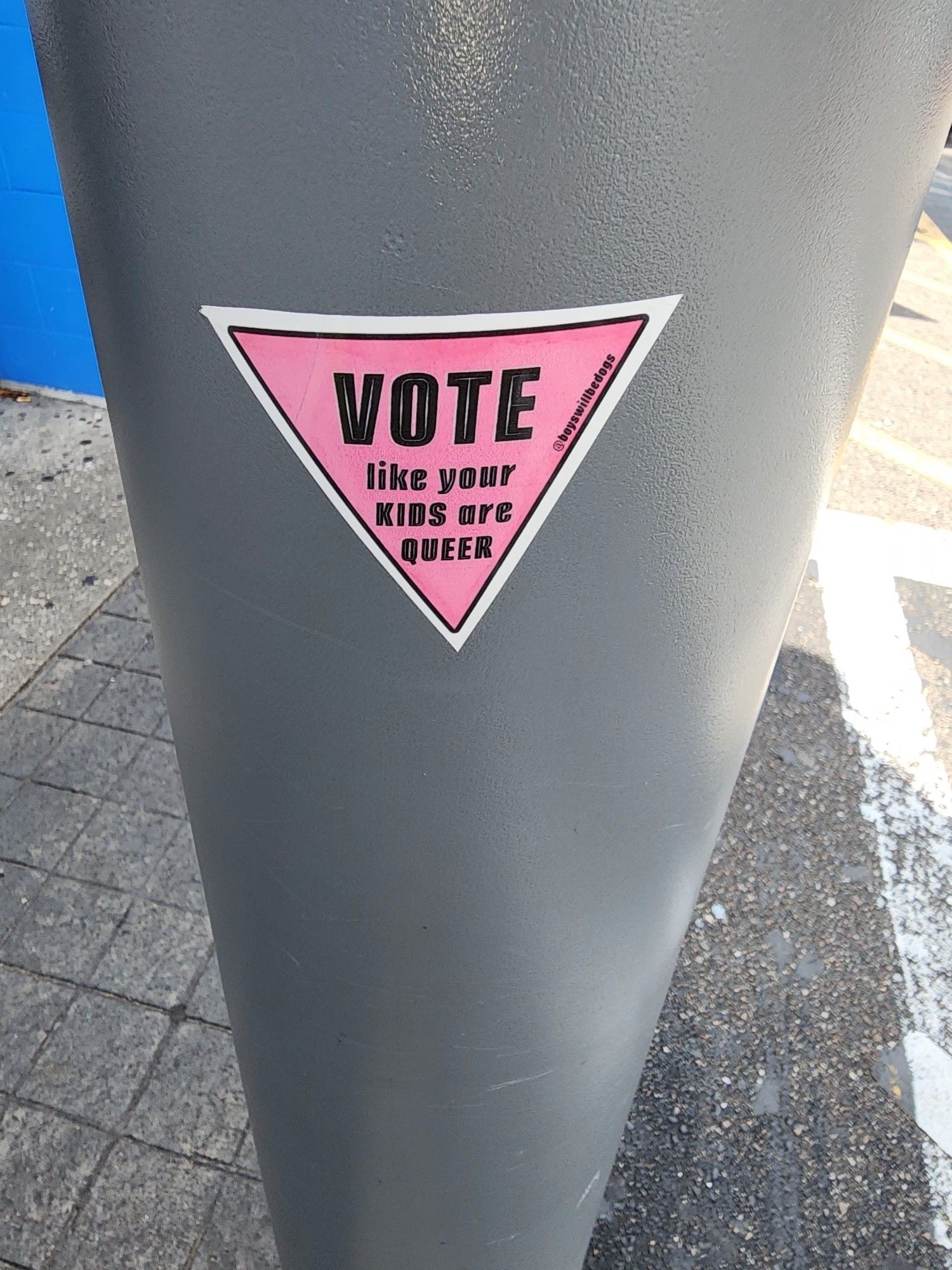 a pink triangle sticker with giant black letters that say vote and the remaining letters say like your kids are queer.