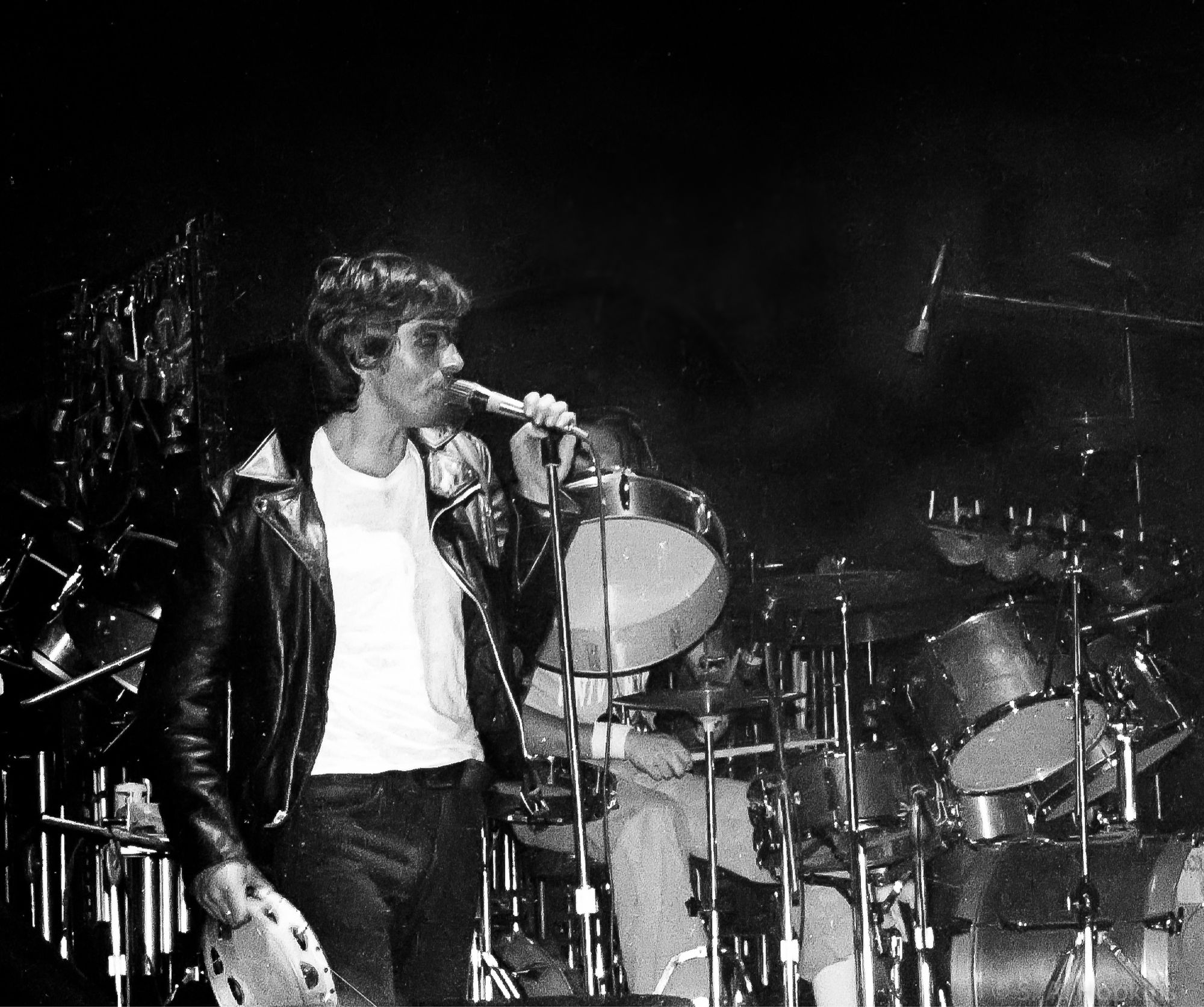 Black and white photograph of a young Peter Gabriel on stage, singing.