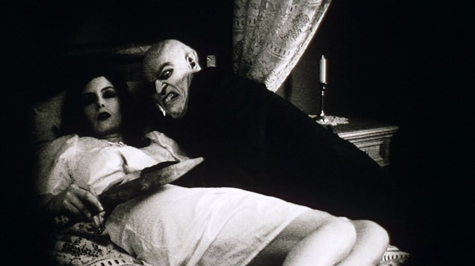 Willem Dafoe in character as Max Schreck himself playing Nosferatu, attacking a female character / actress lying on a bed