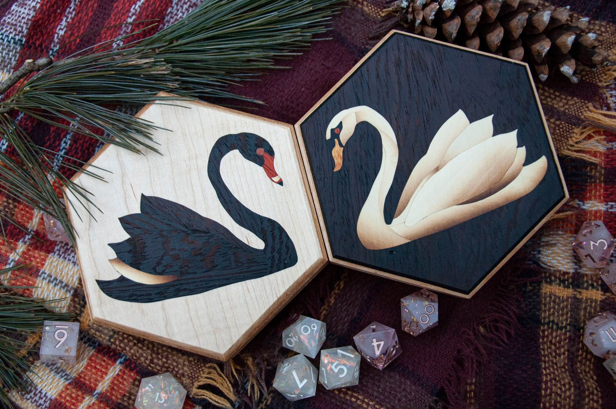 Two hexagonal dice boxes, one with a marquetry black swan against a white background, and the other with a marquetry white swan against a black background. They are facing each other to create a mirrored but contrasting visual. 