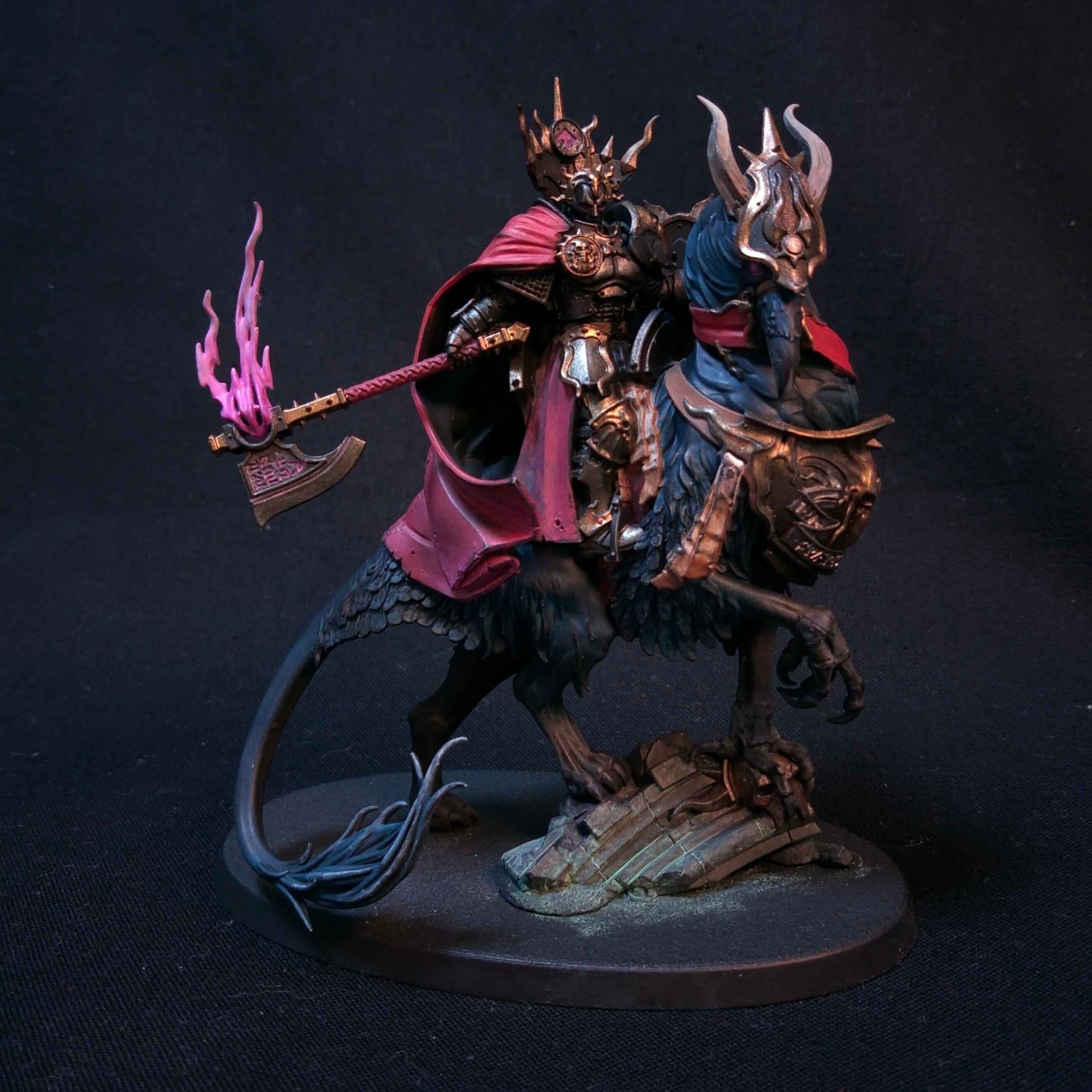 Lord with black armour and gold trimmings, with a big red cloak, wielding an axe ablaze with purple flames. Lord is on a dark blue Gryphstalker mount.