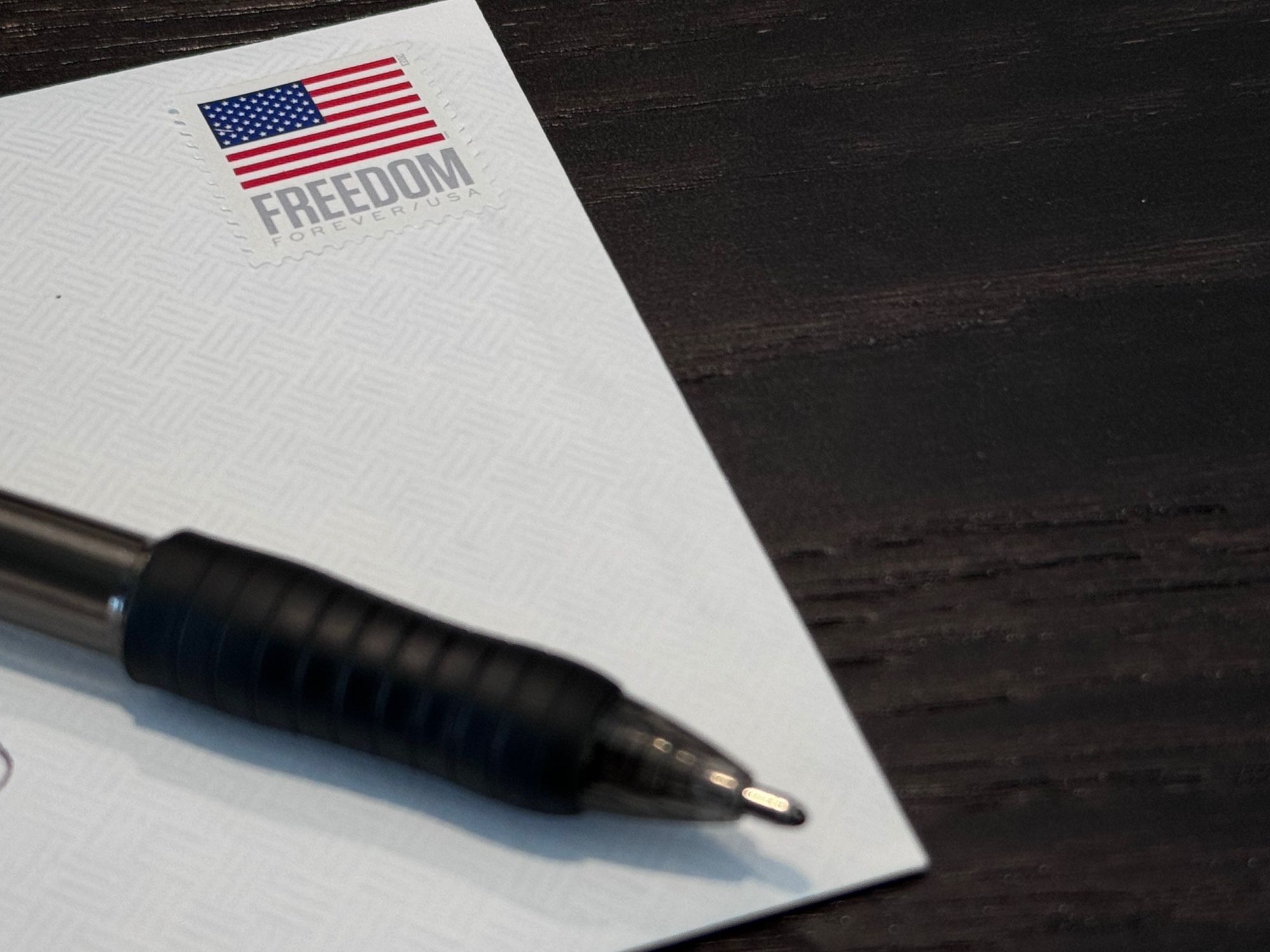 A picture of an envelope with a pen on top. In the upper right corner the envelope is a stamp with an American flag and the word FREEDOM underneath.