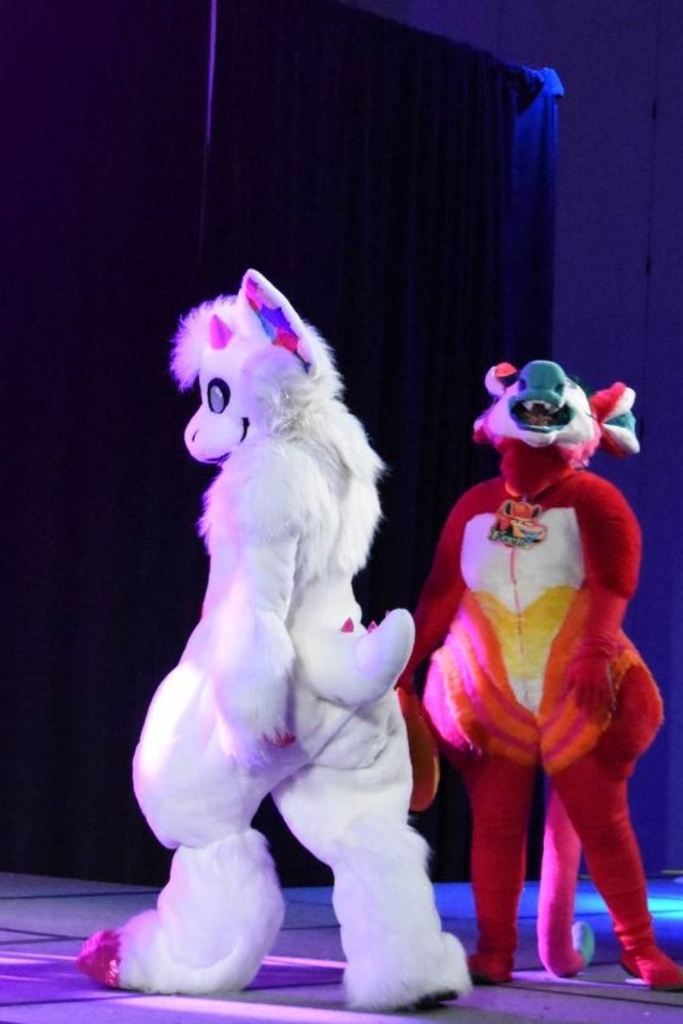 Gay dragon and deer dancing on stage. Dragon faces away from crowd but turns head back all dramatic. Deer is all mouth. 