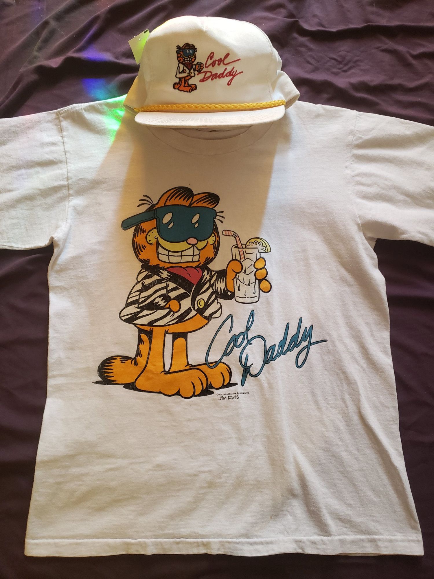 a hat and a shirt featuring garfield wearing a blazer and sunglasses with the words "cool daddy" next to him