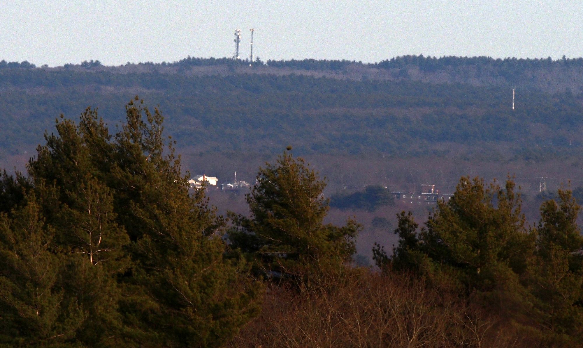 Two cell towers, 433 Clapp Rd, Scituate MA photographed from Buck Hill.

Directly below the towers are two houses, 180 and 187 Westminster St, Weymouth MA. To the right of the houses is Weymouth Place Apartments, 580 Middle St, Weymouth MA.

At the middle right of the frame is what looks like it might be an antenna. It is located at the Hingham Hull Water Treatment Plant, 900 Main St. Hingham MA.