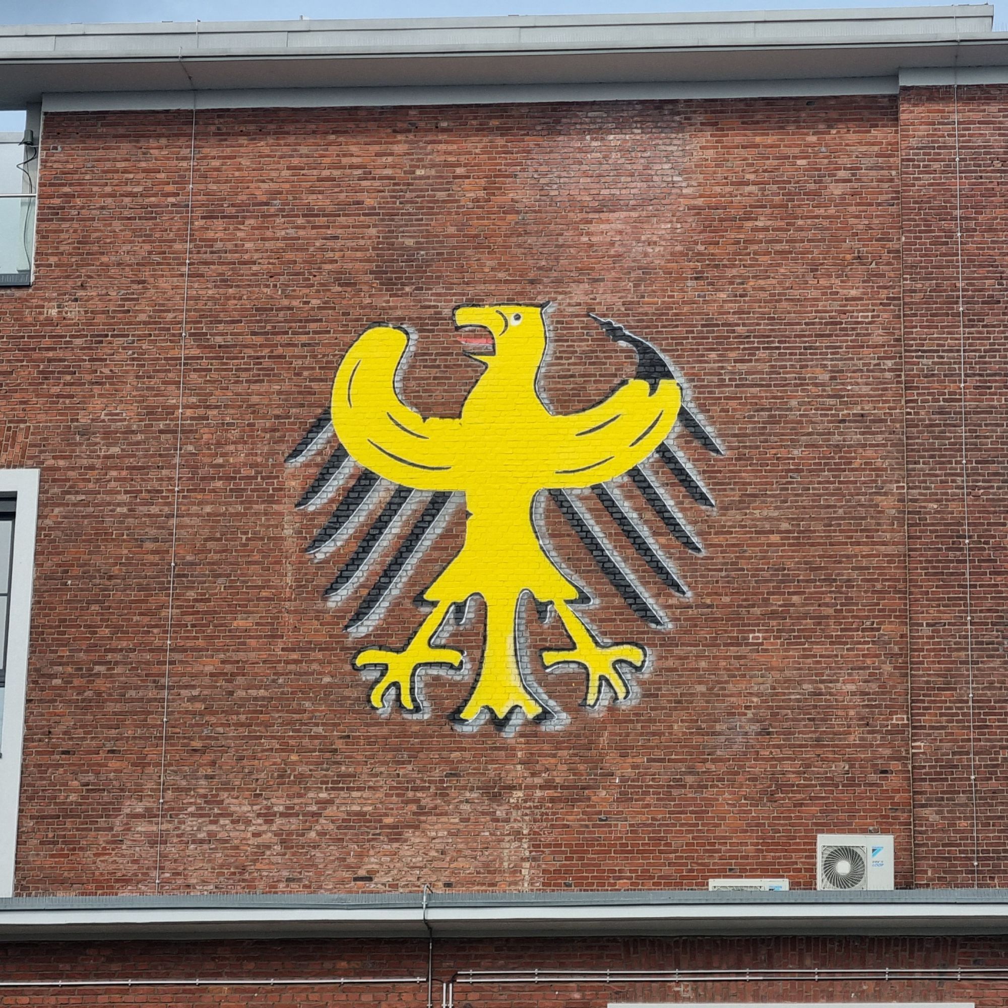 Streetart. Gelber Adler auf einer Ziegelwand. Symbolisch für die Flügelknochen eine Banane.