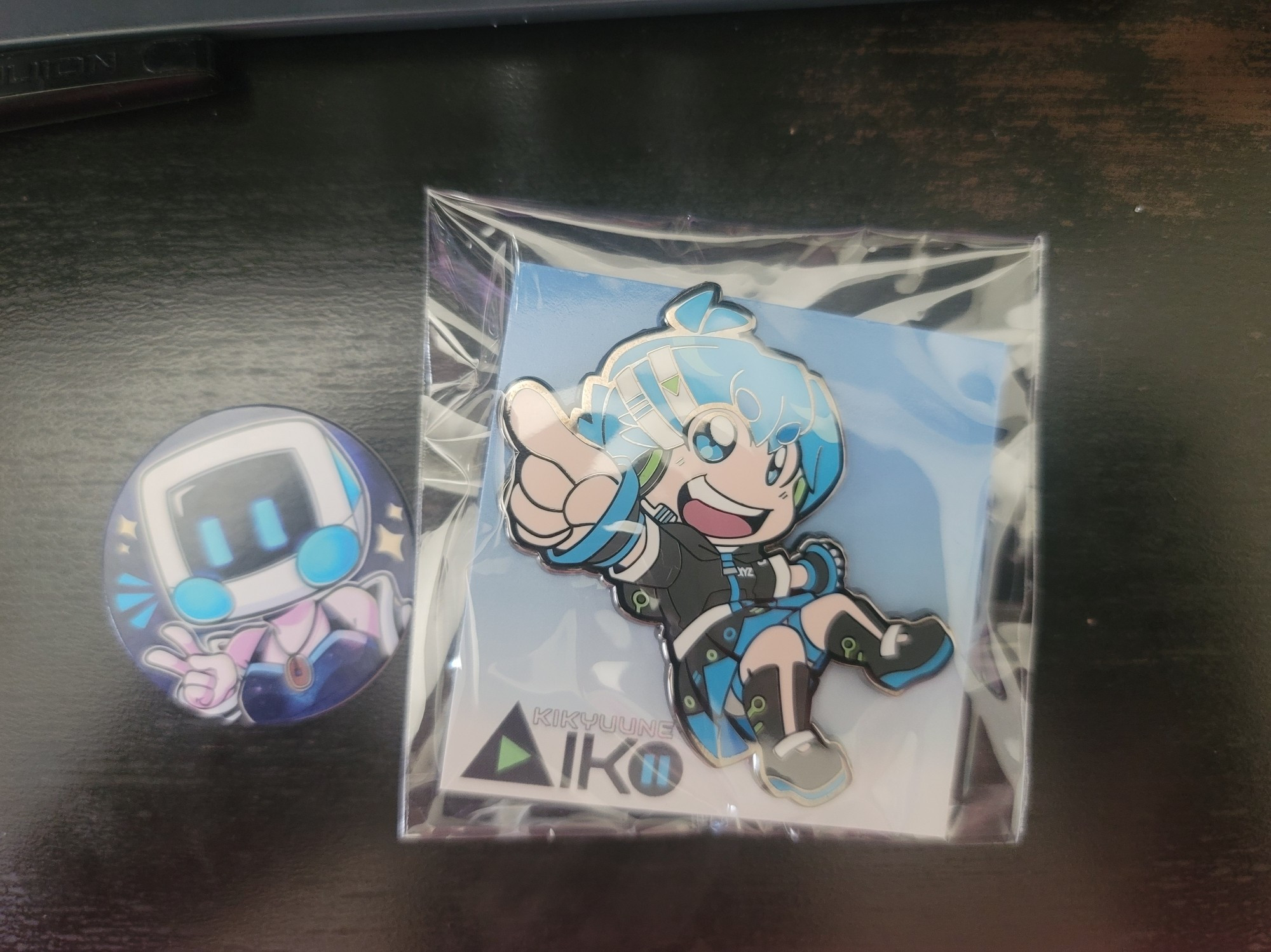 An chibi Aiko Kikyuune enamel pin! Aiko is Myst's UTAU. To the pin's left is a colored, card disk featuring Myst's sona on the front, and her socials on the back.