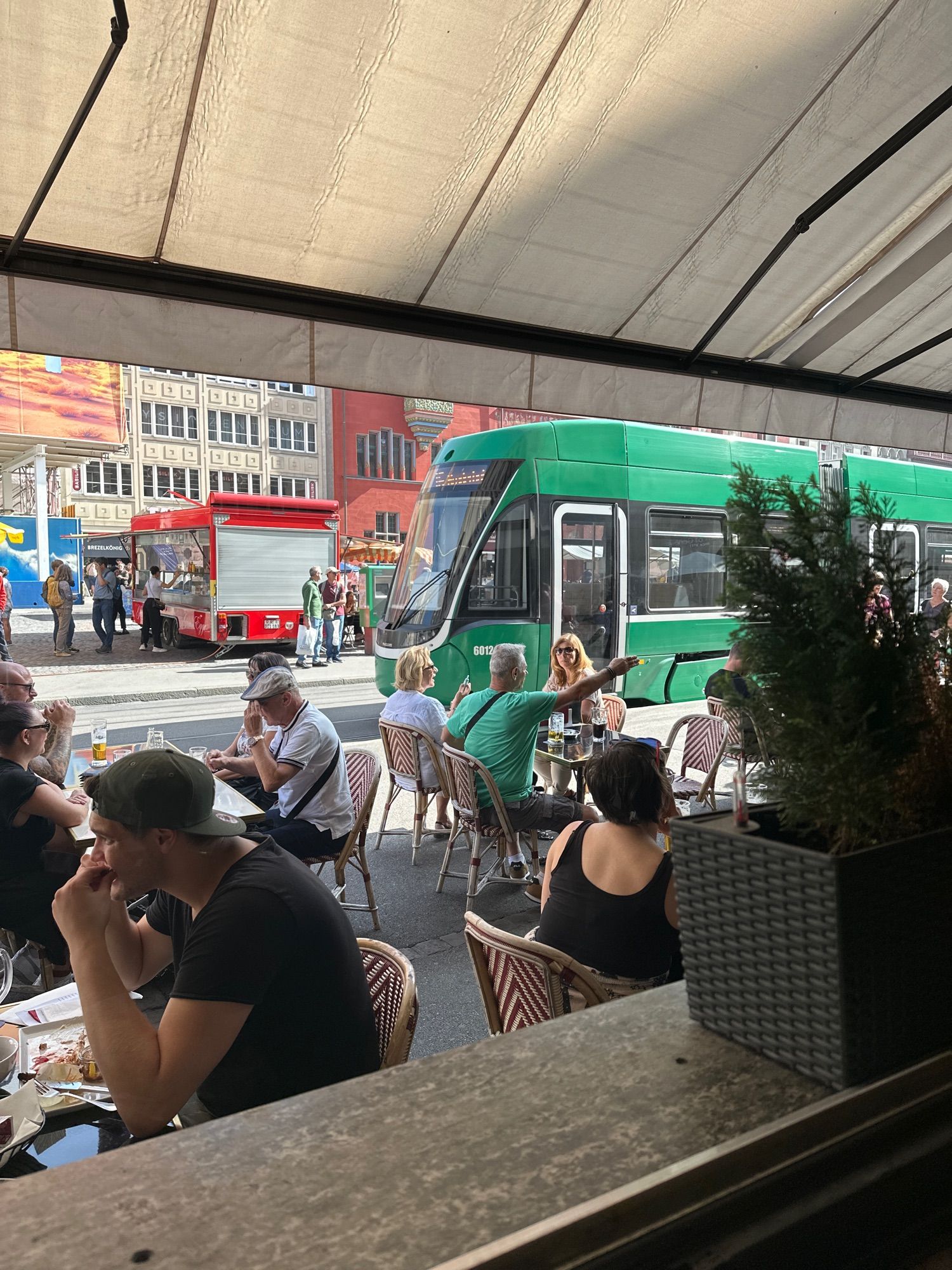 Picture of outside from a Swiss cafe with people eating and a green cable train moving out of the frame.