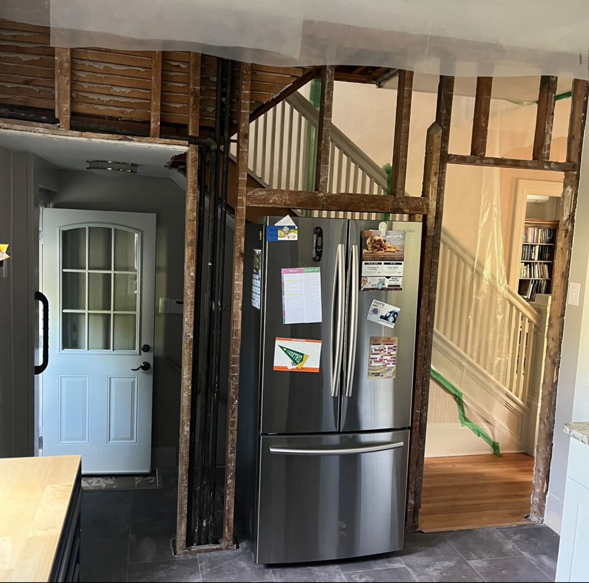 The same staircase seen from the side. The grand old staircase rises bottom right to top left. The stripped wall is a complicated lattice of doorways, studs, pipes, and plaster and lathe. Again, the refrigerator is right in the middle of everything, blocking the passage from front to back.