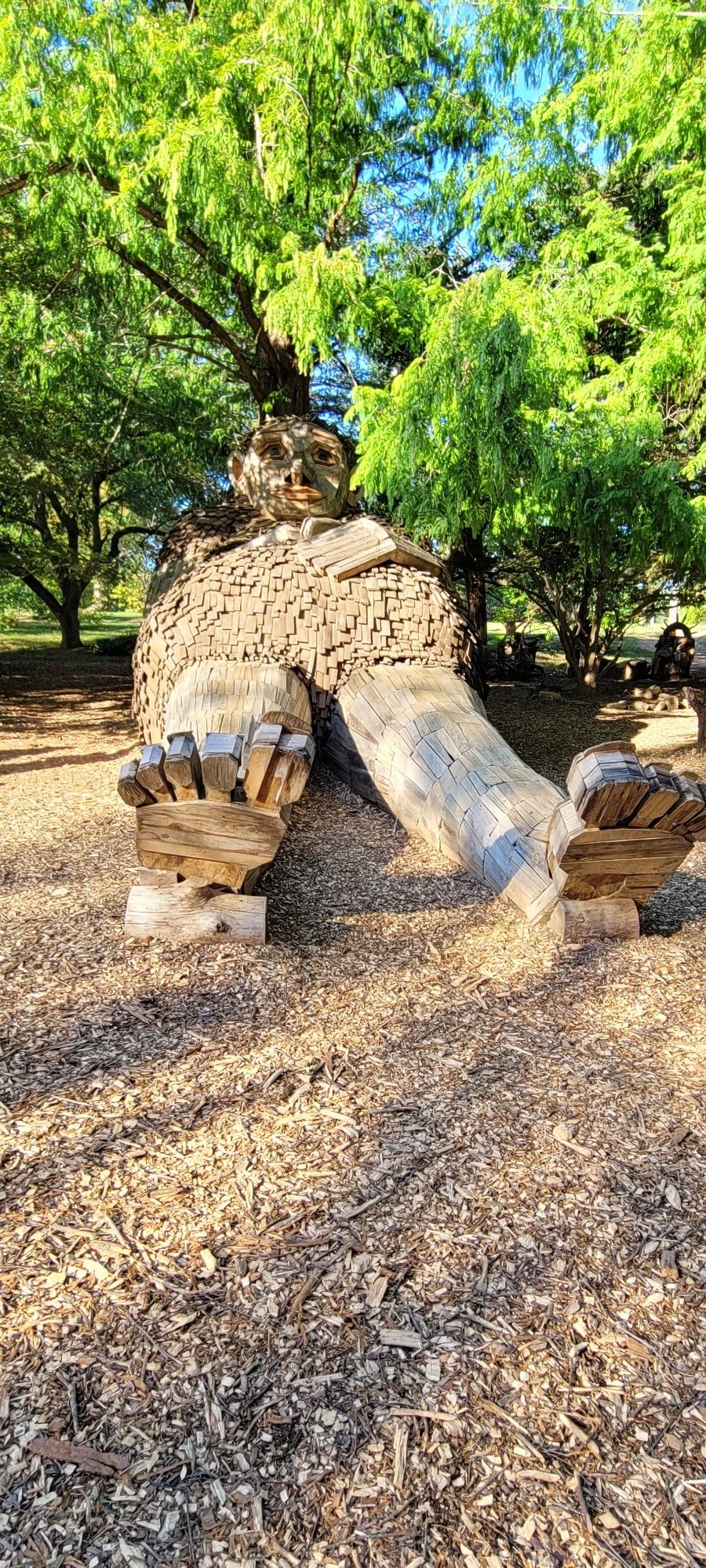 A wooden statue of a troll laying down with a hand on its belly