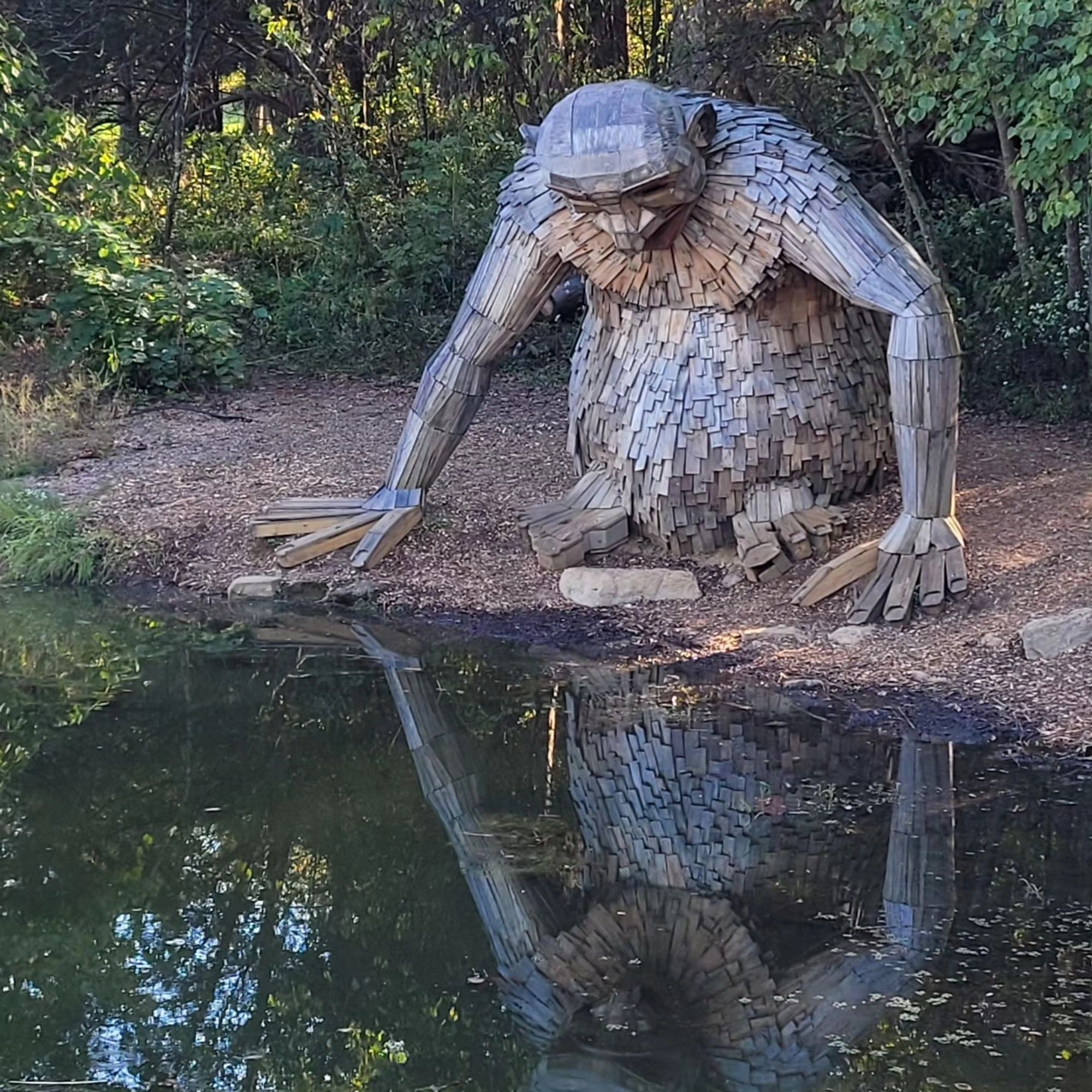 A wooden statue of a troll looking into a pond