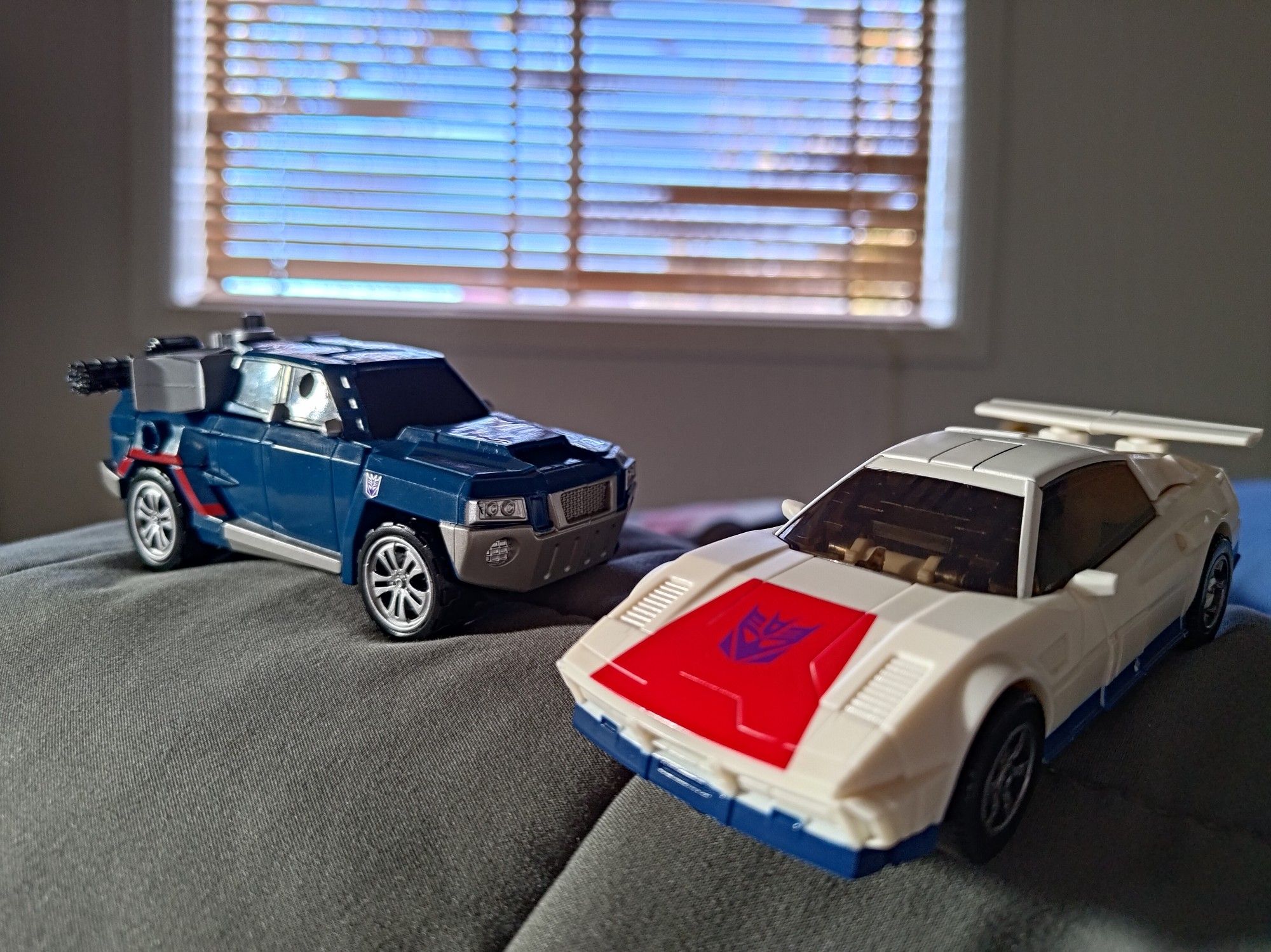 transformers legacy breakdown next to transformers prime takara deluxe breakdown, both in vehicle mode. 
prime breakdown is a pickup truck and legacy breakdown is a stylised sports car