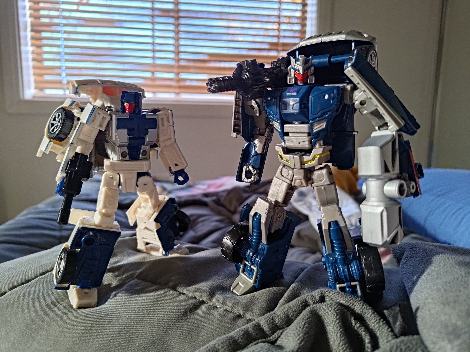 transformers legacy breakdown standing next to transformers prime takara deluxe breakdown, both in robot mode in A stances