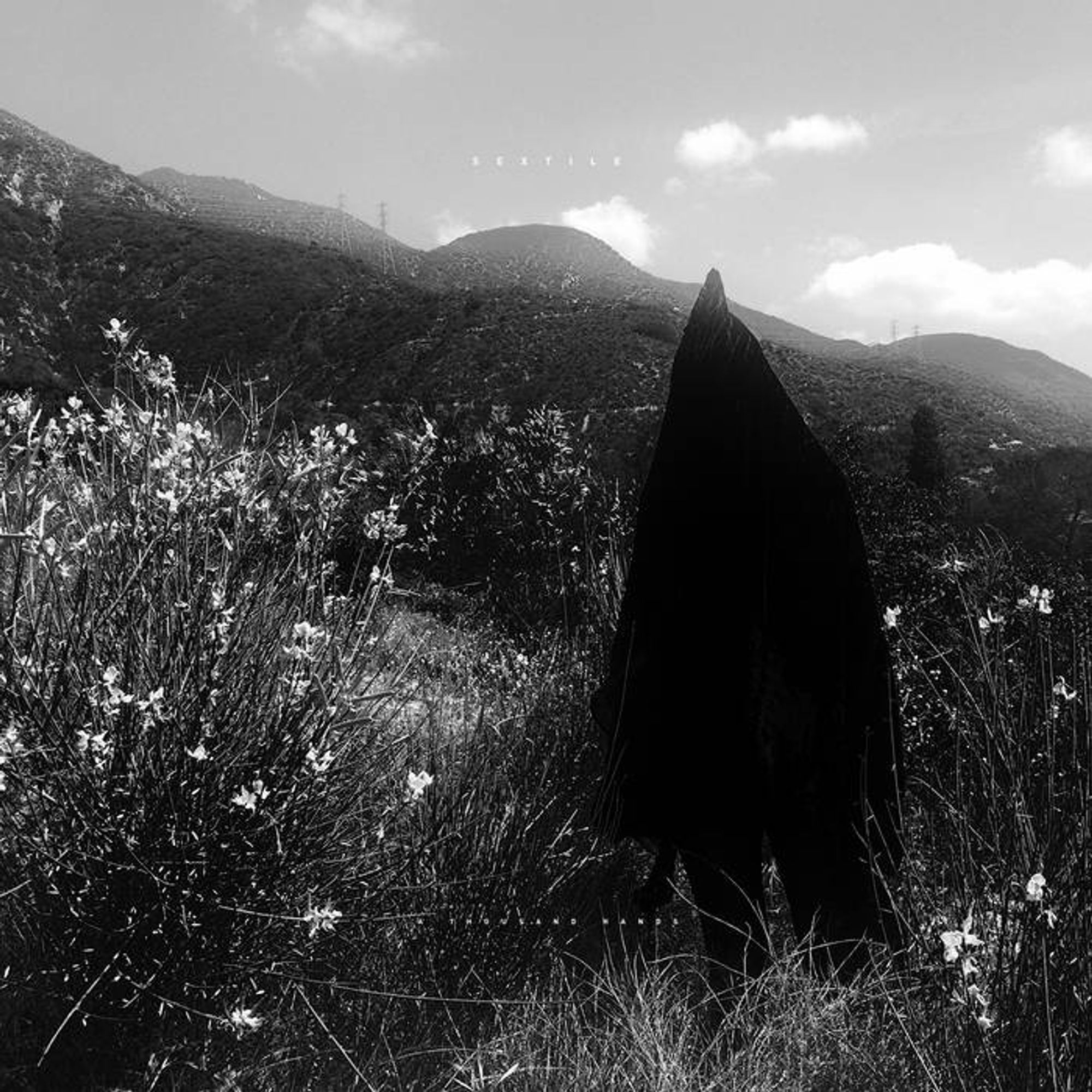 The cover of A Thousand Hands (2015) by Sextile. The picture is a black & white photograph of a grassy hillside. A black-robed figure with a hood covering their face stands in the foreground on the right.