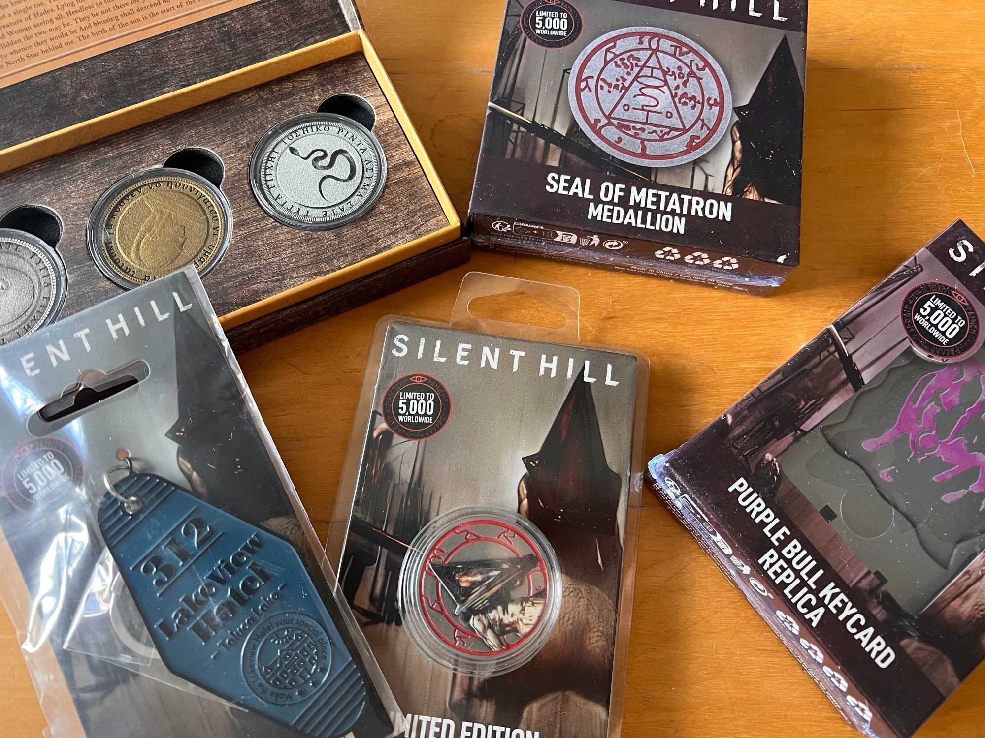 A selection of Silent Hill collectibles: The Rm 105 coins, a key fob from Lakeview Hotel, A PH coin, a Seal of Metatron medallion, the purple bull keycard replica.