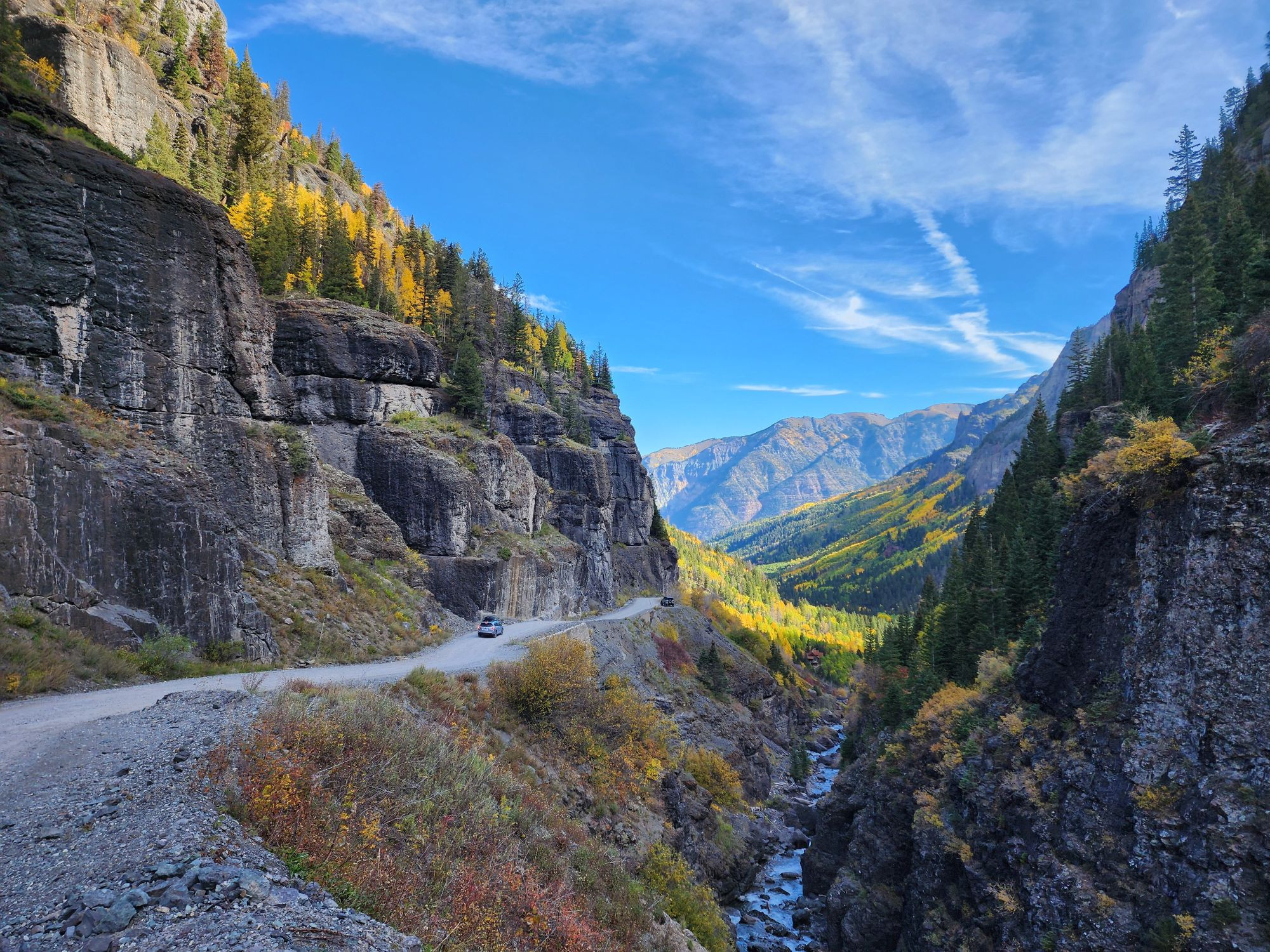 A picture of cars driving down a canyon road with the San Juan mountains in the background