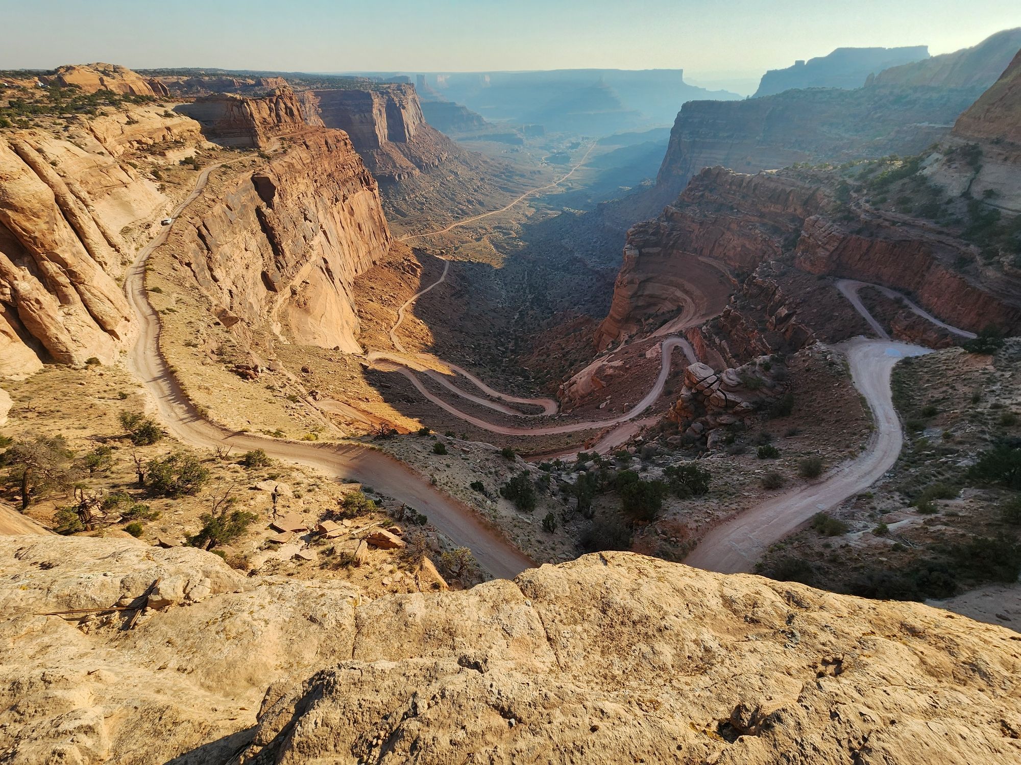 A photo looking down on Shafer Trail in Canyonlands National Park. The photos depict a switchback road going down to a canyon floor at 9am