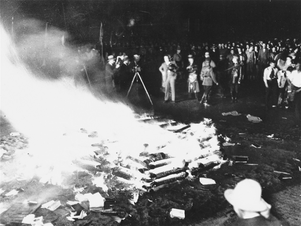 Black and white photo of books burning a blaze in the street with a crowd around watching