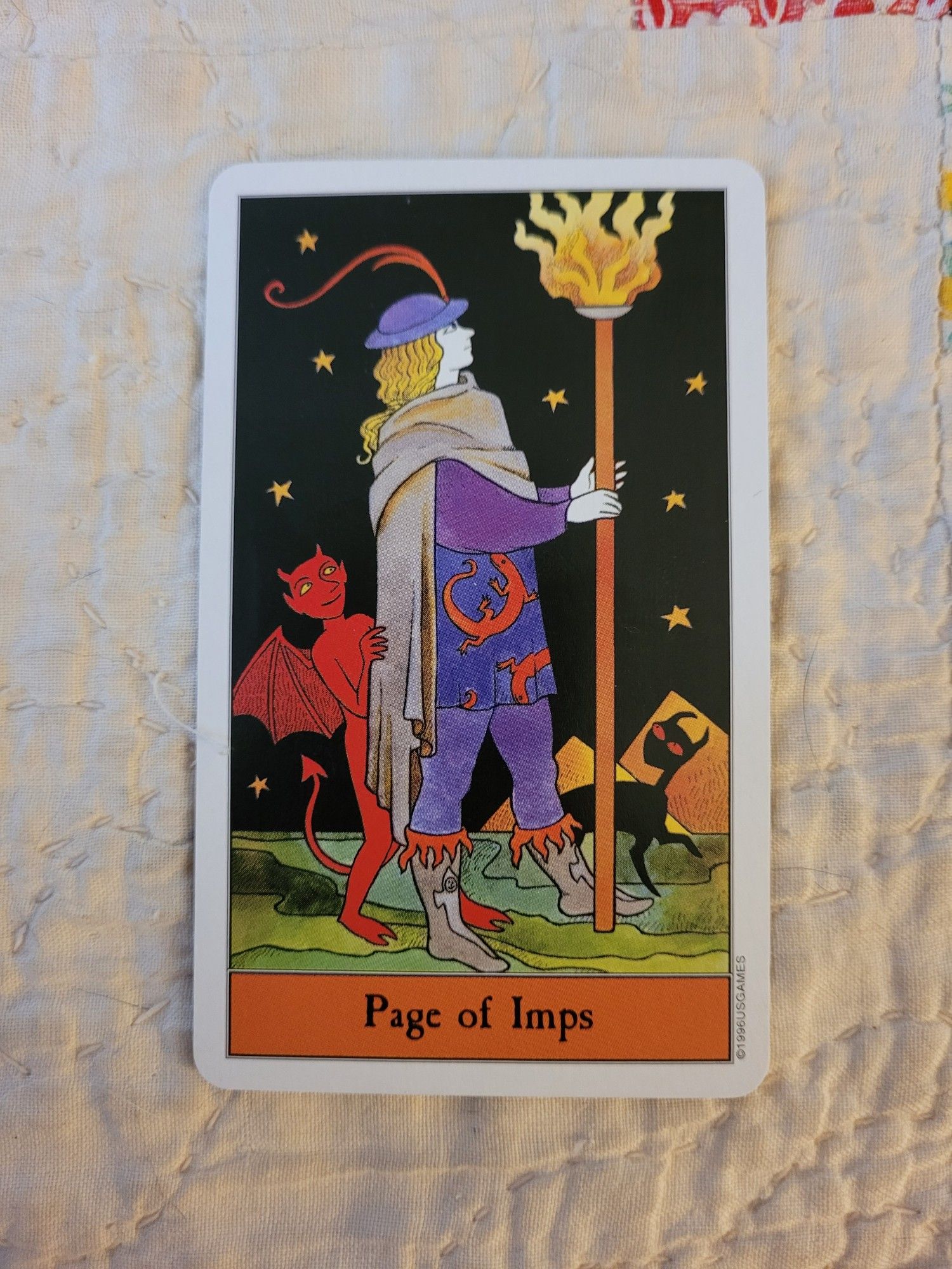 Page of Imps, from Kipling West's Halloween Tarot. Equivalent to the Page of Wands and very similar to the Waite-Smith imagery, showing a young blond person holding a staff as if getting everyone's attention before an announcement. This card sets the scene at night under a starry sky, and the staff is also a torch.