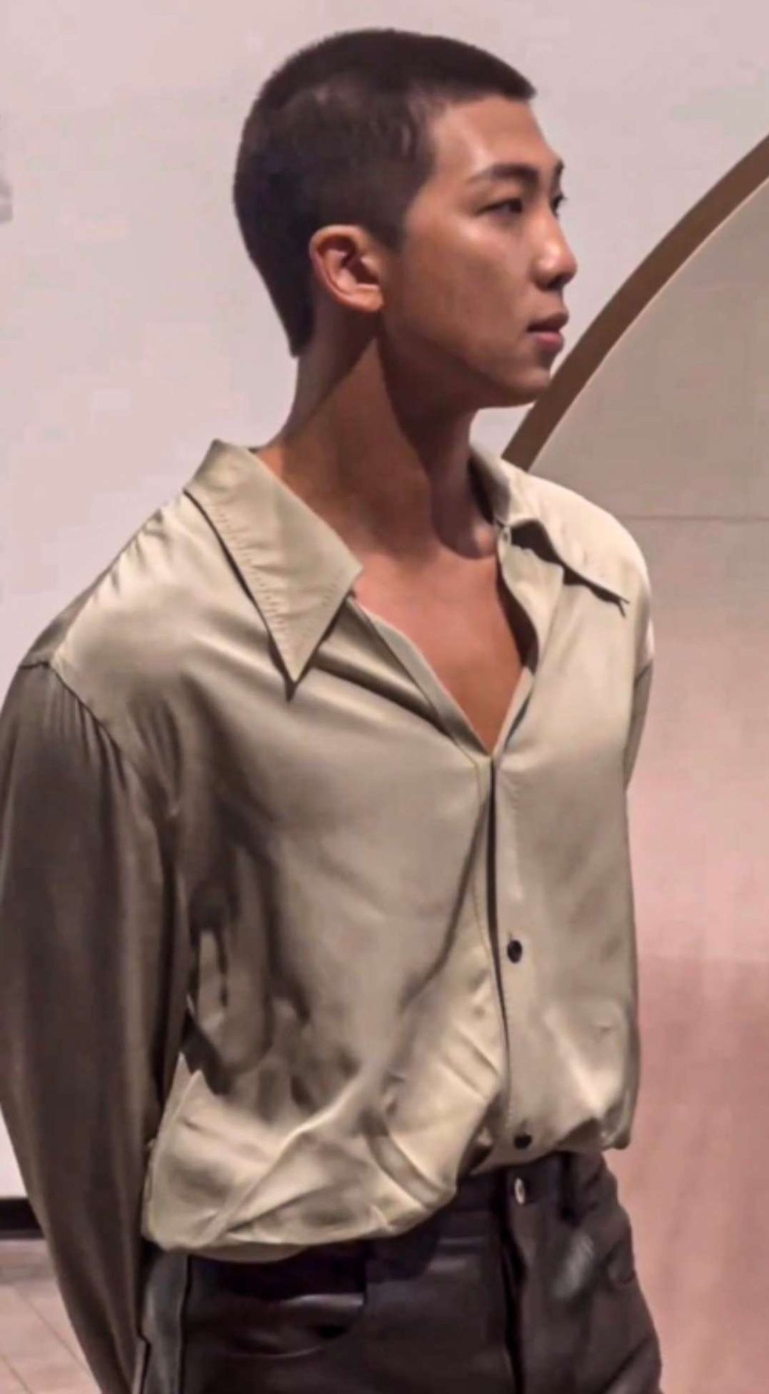 RM of BTS with a buzz cut wearing a silk Bottega Veneta shirt and leather Bottega Veneta pants.