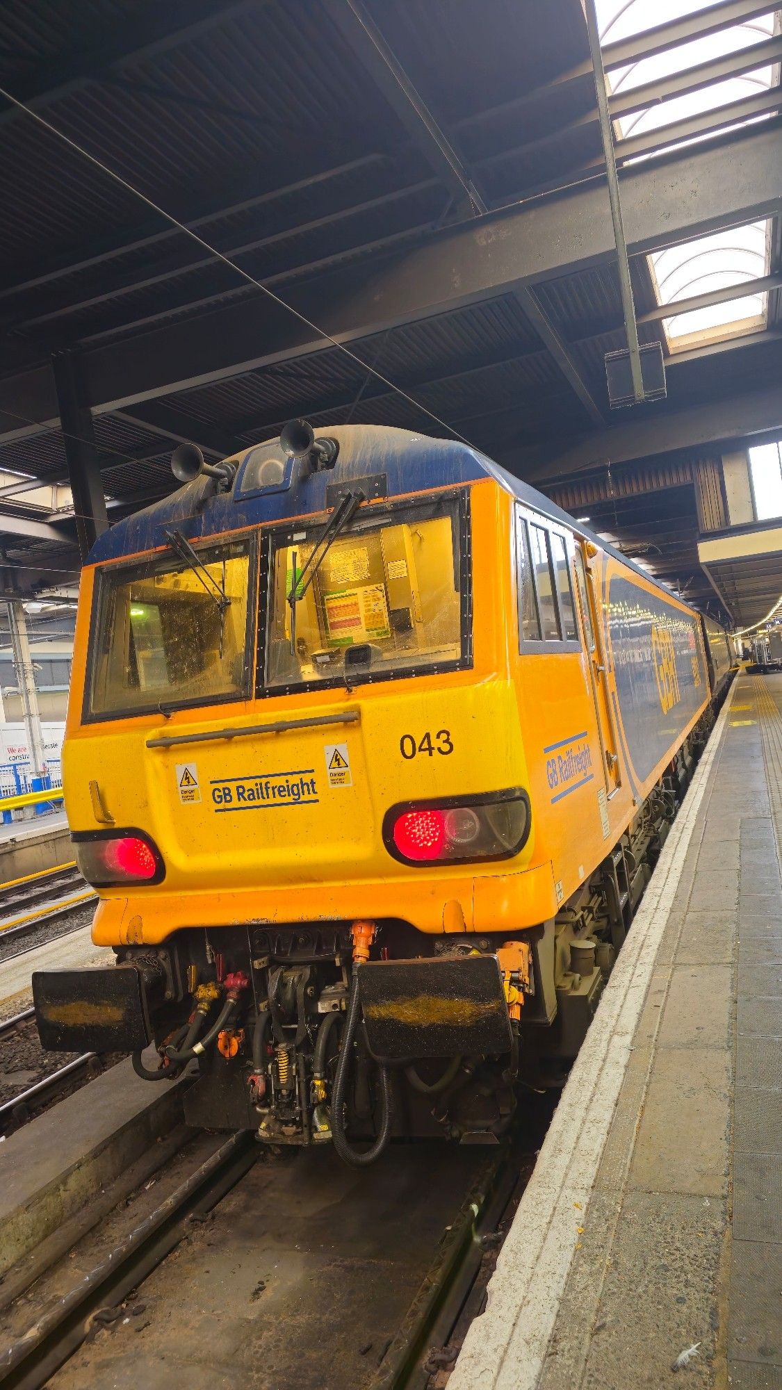 Class 92 loco 92043, in orange and dark blue GBRf livery, rests at the buffer stops at London Euston station after hauling the Highland Caledonian Sleeper.