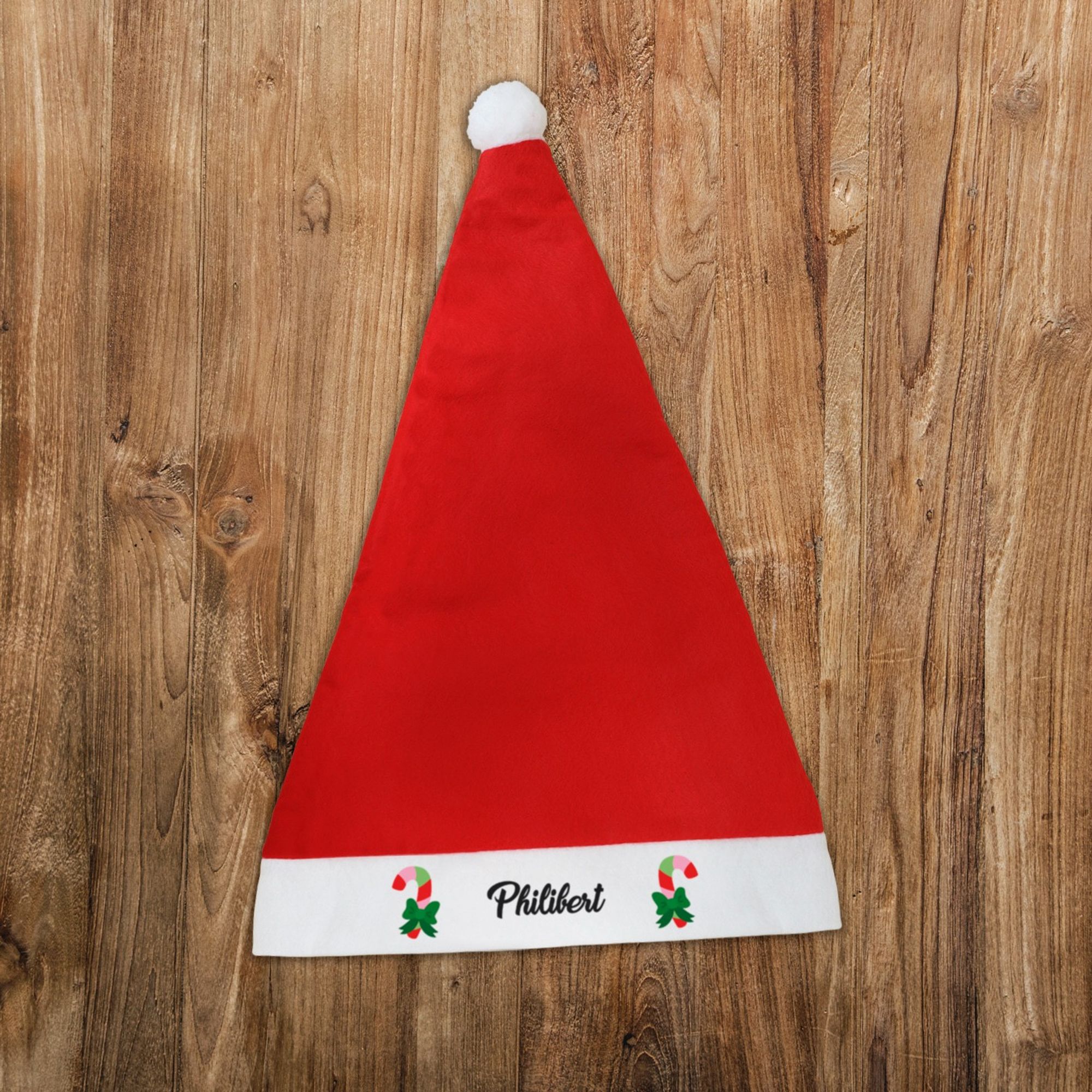 Bonnet de Noël rouge avec un pompon blanc et personnalisé avec le prénom de votre choix entouré de sucres d'orge colorés.