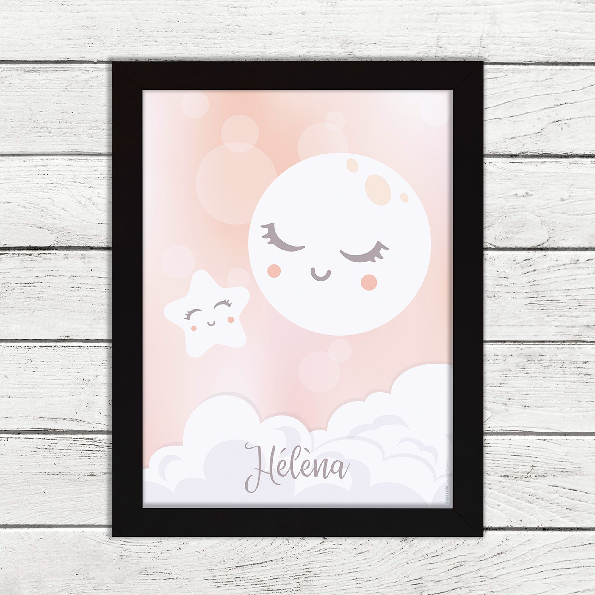 Affiche personnalisée avec prénom pour chambre d'enfant ou cadeau de naissance représentant une lune ronde et une étoile toute deux souriantes sur fond rose pastel, présentée avec l'option cadre noir.