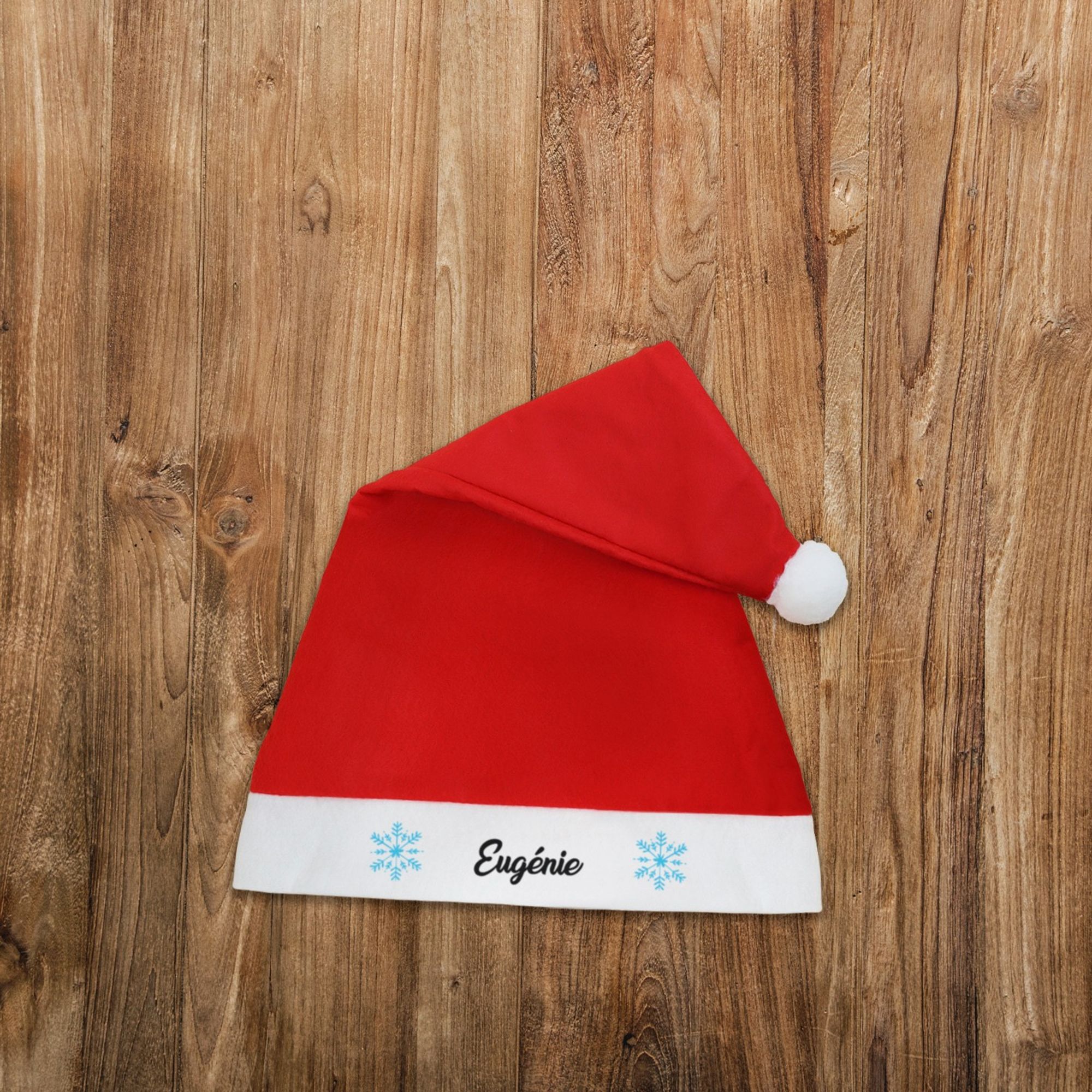 Bonnet de Noël rouge avec un pompon blanc et personnalisé avec le prénom de votre choix entouré de flocons de neige.