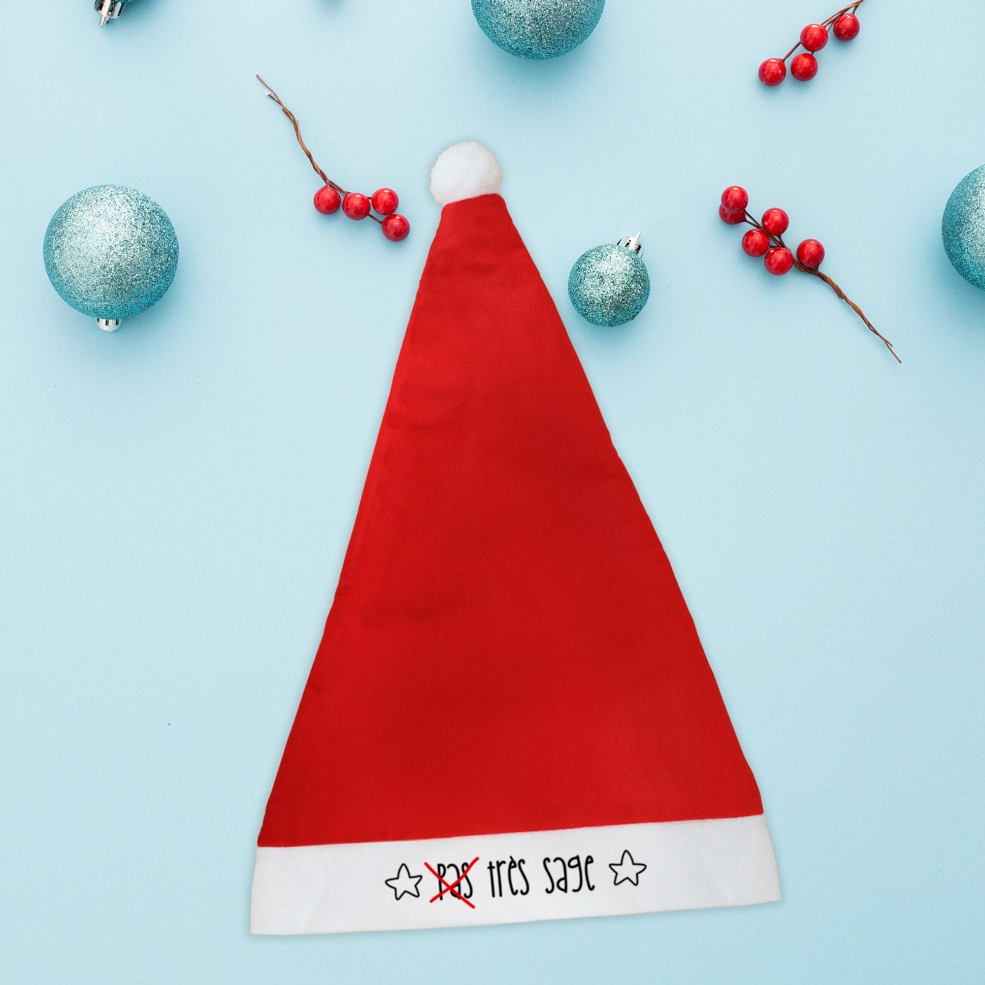 Bonnet de Noël rouge avec pompon sur lequel est écrit le texte plein d'humour : pas très sage, mais le pas est barré.