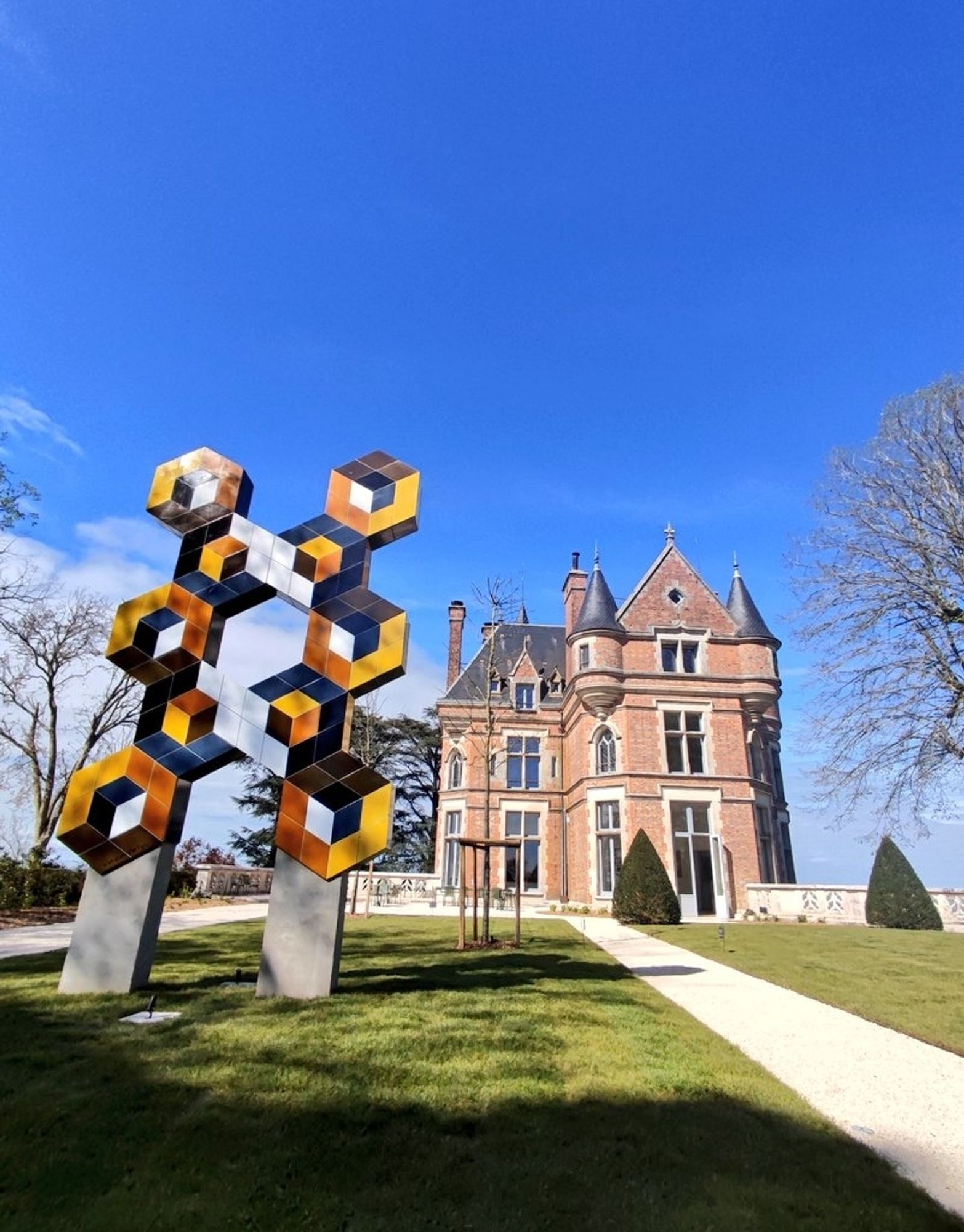 Vue de la terrasse sur le  château en brique du 19ème et une œuvre de Vasarely sur la pelouse