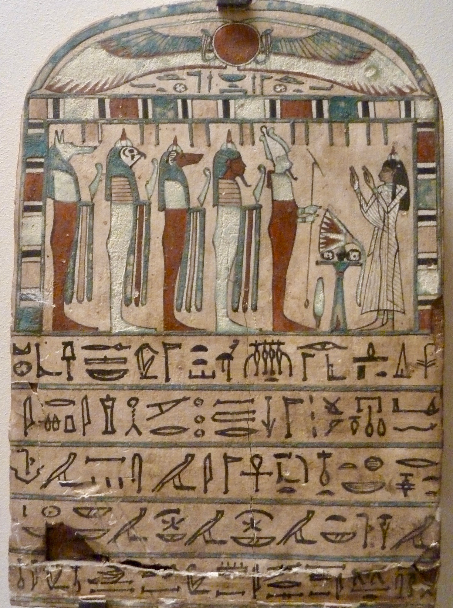 Photo of a tablet that looks like a sign, with a picture at the top and hieroglyphs at the bottom. In the picture, there is a figure (I believe it’s a woman) on the right in a white gown with arms raised. There is something on a little table or stand in front of this figure). A line of figures has formed on the other side, each holding something. One is Horus, I think (falcon head), and a couple have dog heads (one brown, one white). Two other figures are human, one brown and one white. In my decidedly amateur and fairly ignorant opinion, the white one looks like a priest and the brown one looks like a pharaoh. I may be wrong. Unfortunately, I did not get the details of this piece, so I do not know its age. 