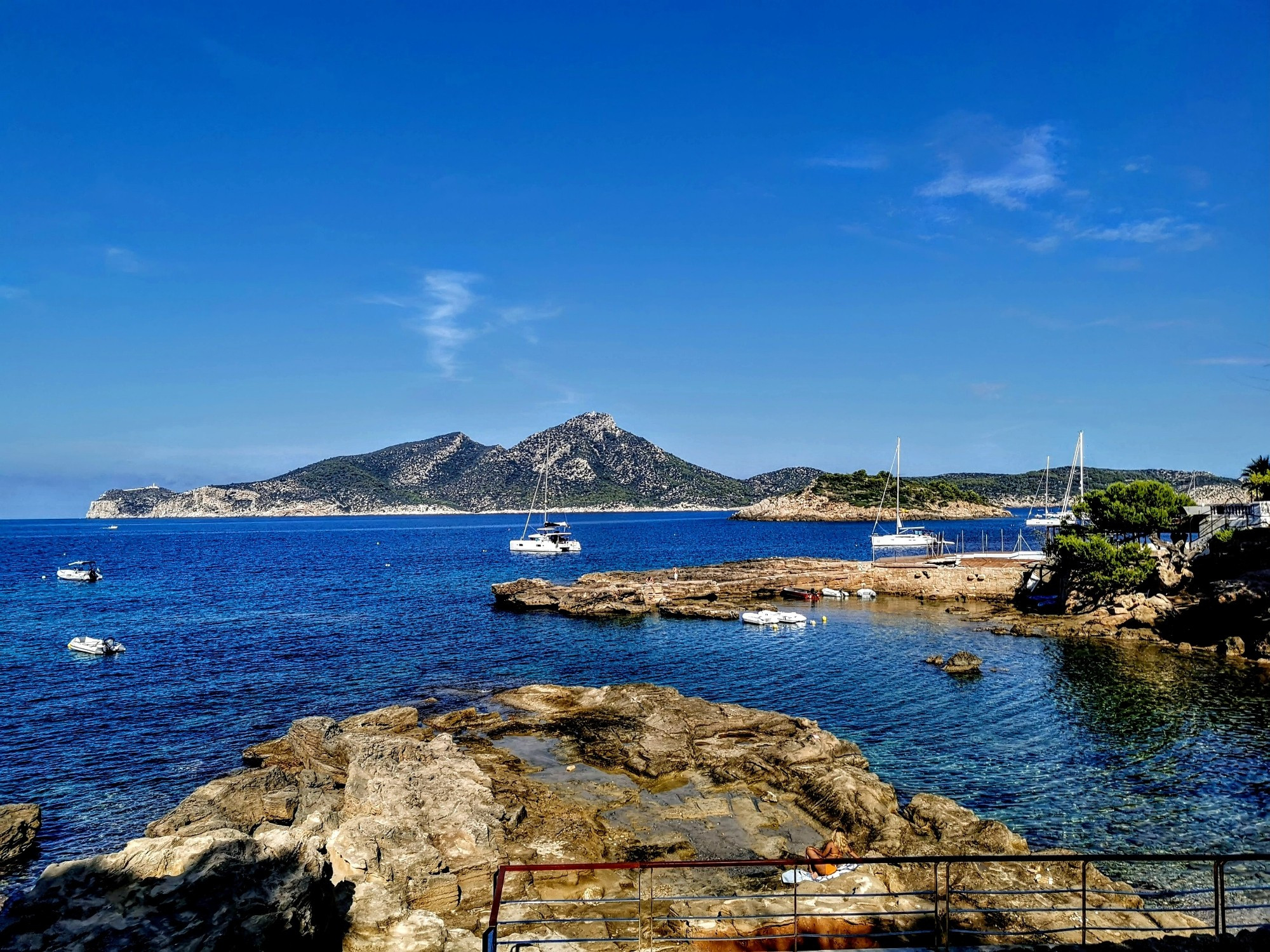 Blick auf eine Bucht und eine Insel mit Felsen und ankernden Jachten im Vordergrund